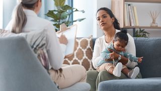 Mother and toddler seated on a couch, in discussion with a medical professional