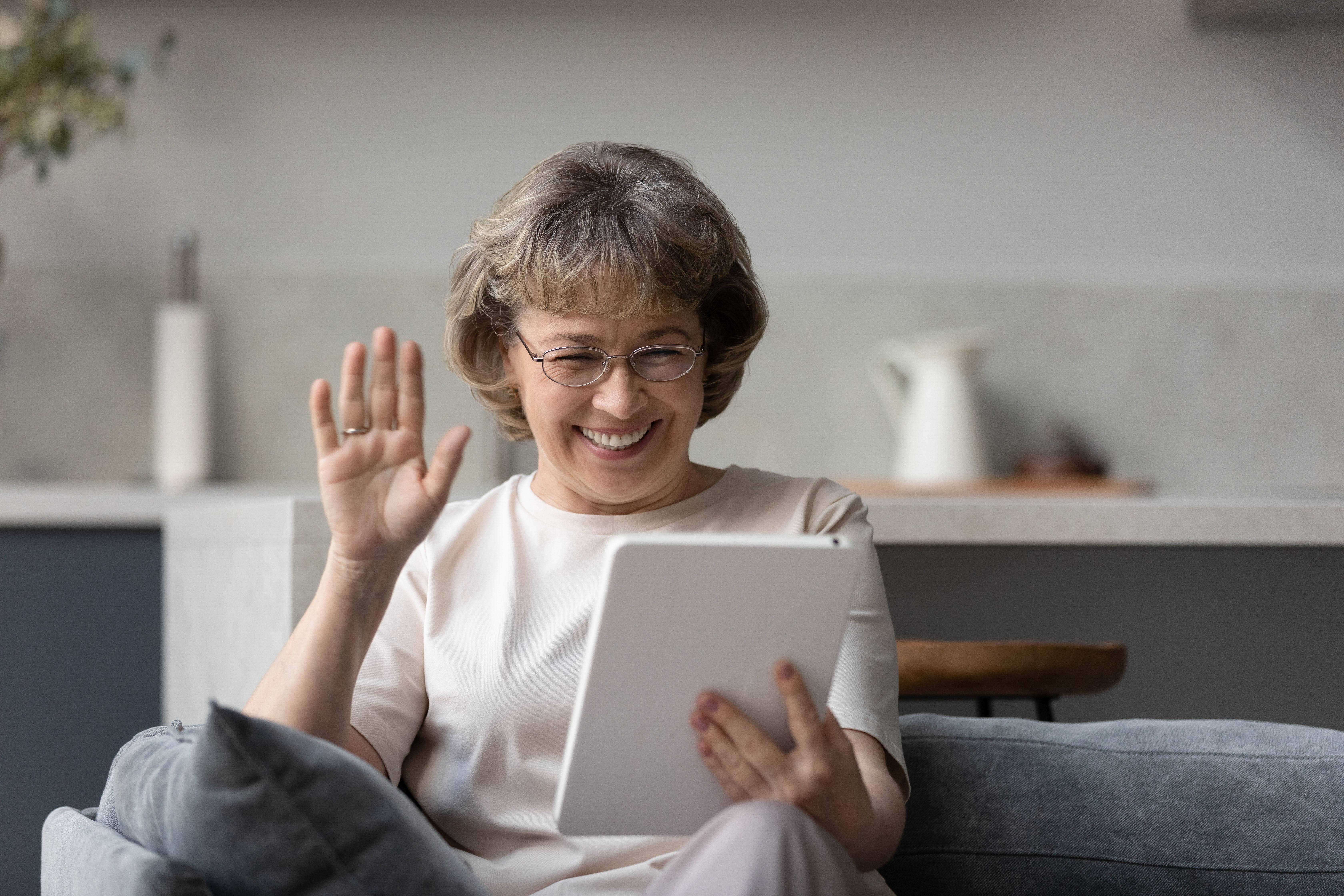 A woman smiling and waving while using her tablet.