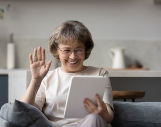 A woman smiling and waving while using her tablet.