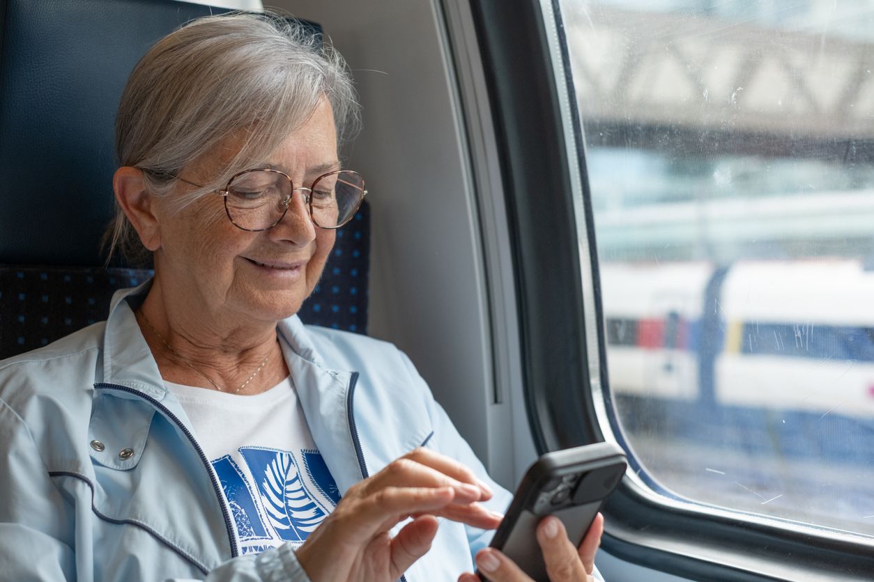 Older woman typing on her phone while sitting on a train
