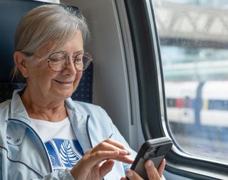 Older woman typing on her phone while sitting on a train