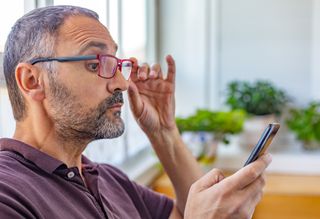 Person shifting glasses to view mobile phone