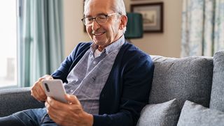 Smiling older person sitting at home using smart phone