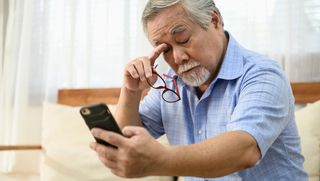 Older person rubbing eyes while looking at smart phone