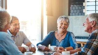 Group of four older people talking and having coffee