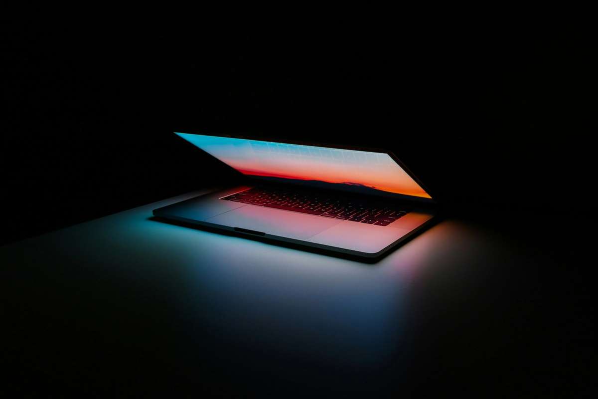 Open laptop glowing with a warm sunset gradient on its screen against a dark background