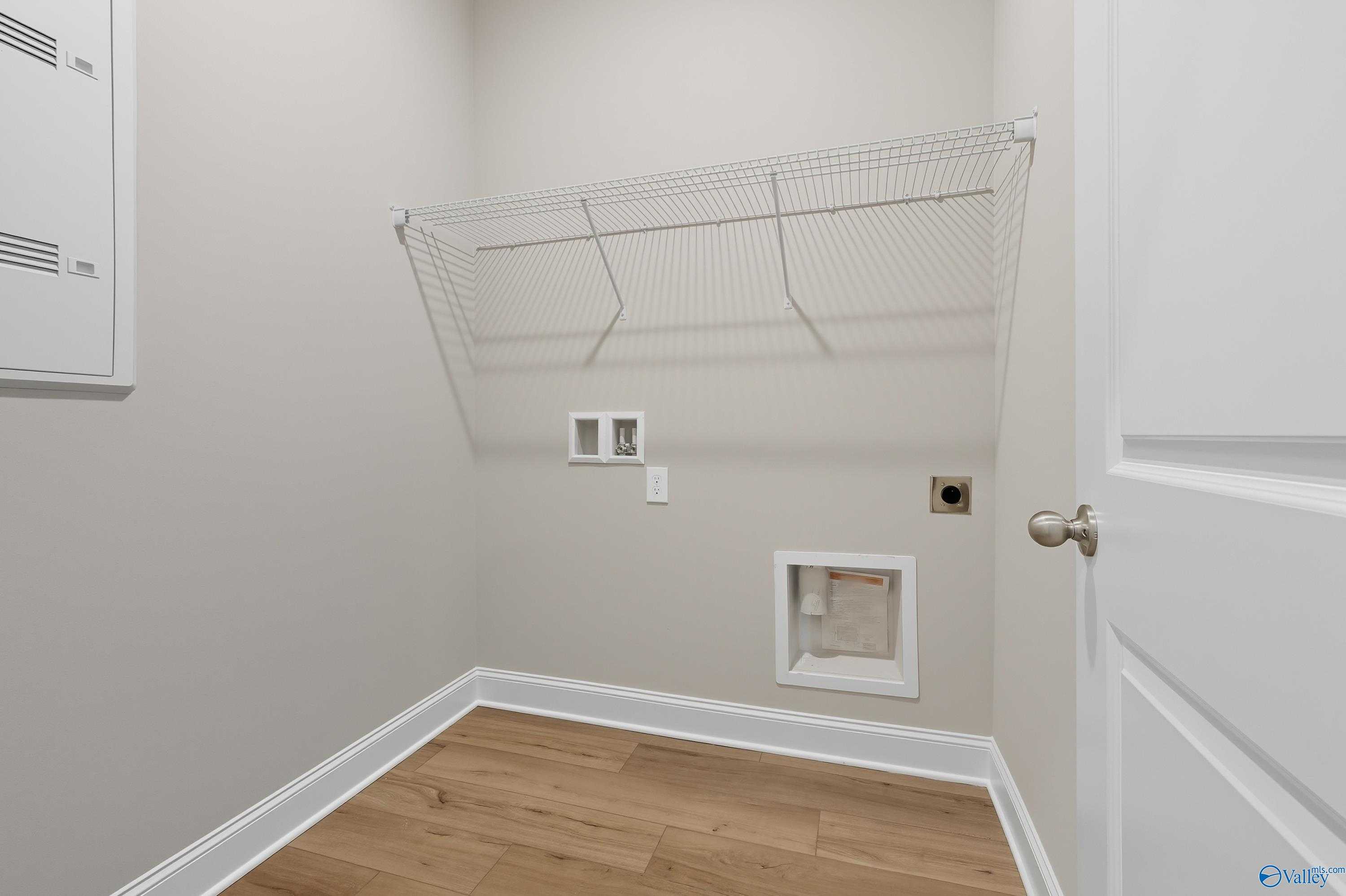 Compact laundry room with wire shelving, washer dryer hookups, and beige walls in The Franklin by Davidson Homes, Meridianville AL