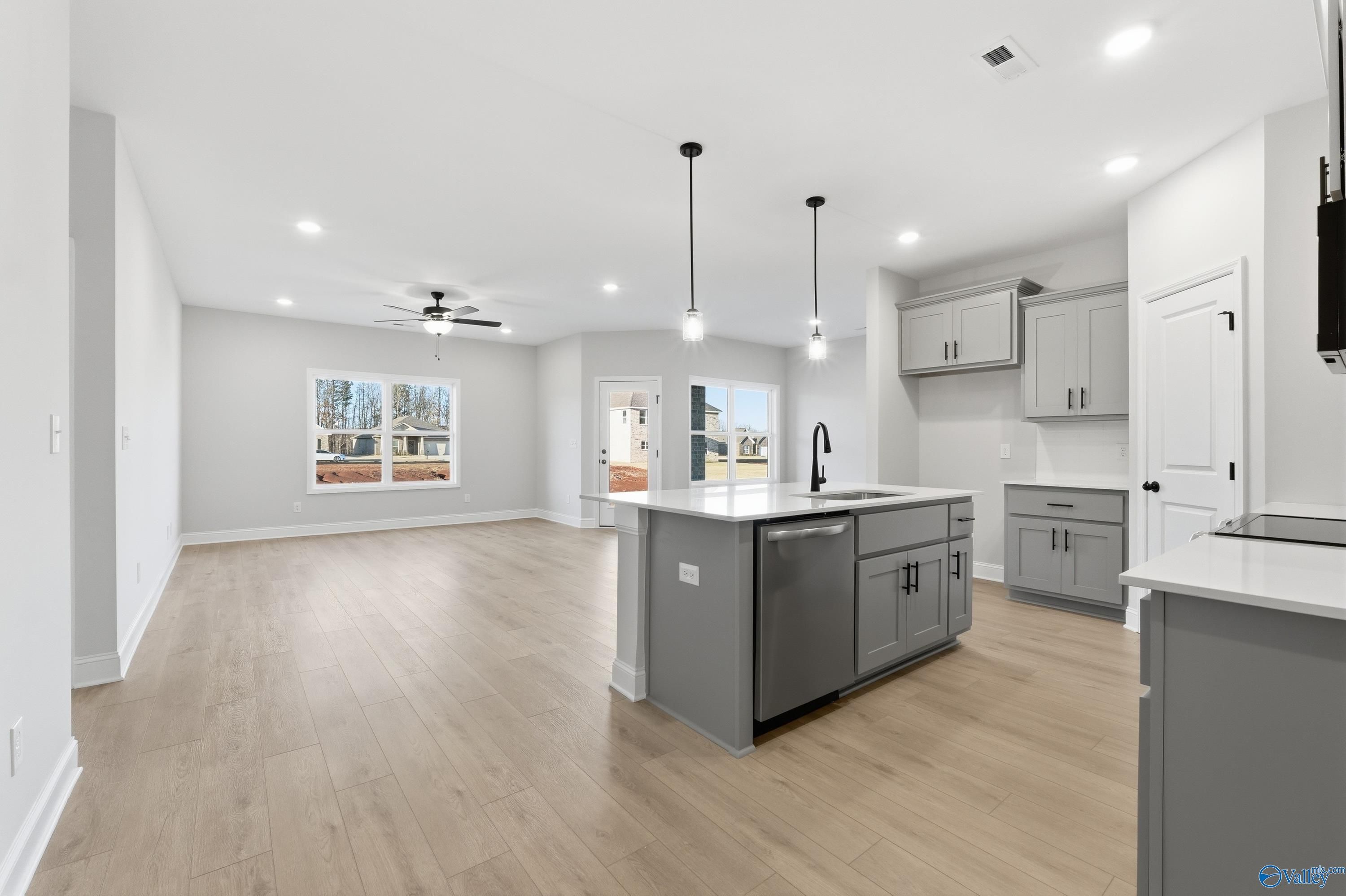 Modern open kitchen with gray island, white cabinets, stainless sink, and hardwood floors in The Daphne C home, Athens, Alabama