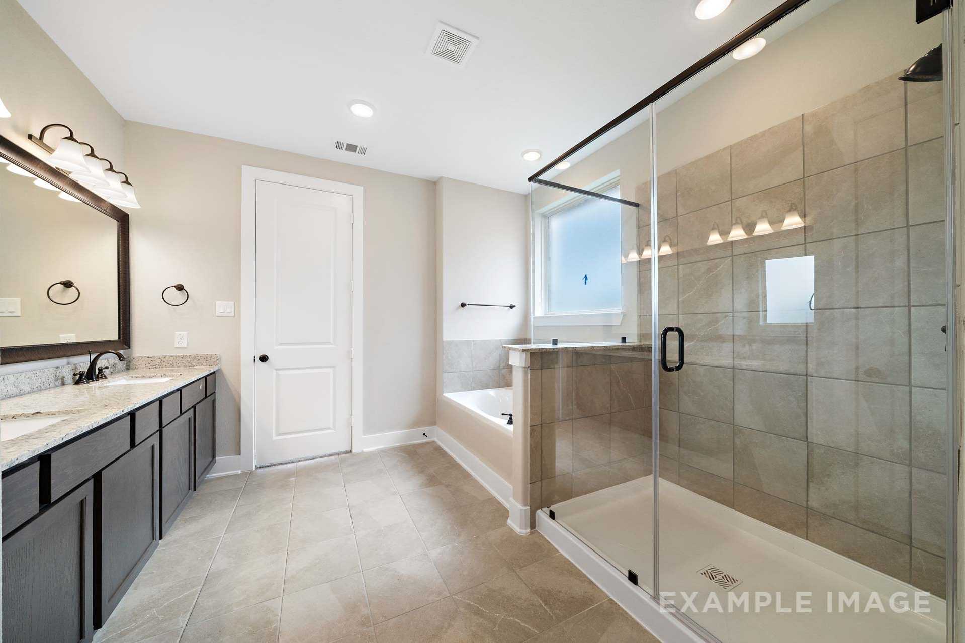 Spacious master bathroom in The Elizabeth A featuring dual vanities, frameless glass shower, soaking tub, and neutral tile