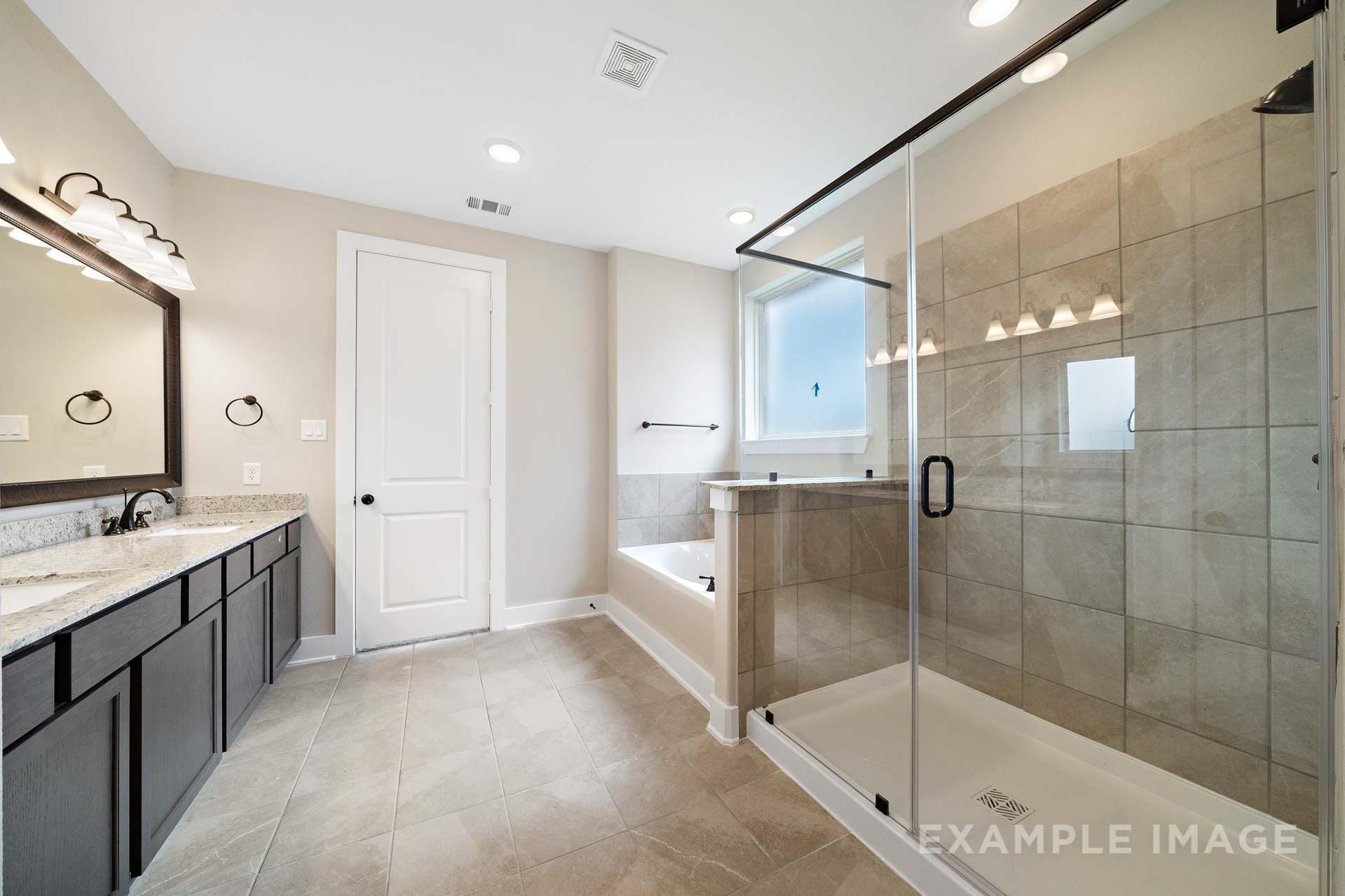 Spacious master bathroom in The Elizabeth A featuring dual vanities, frameless glass shower, soaking tub, and neutral tile