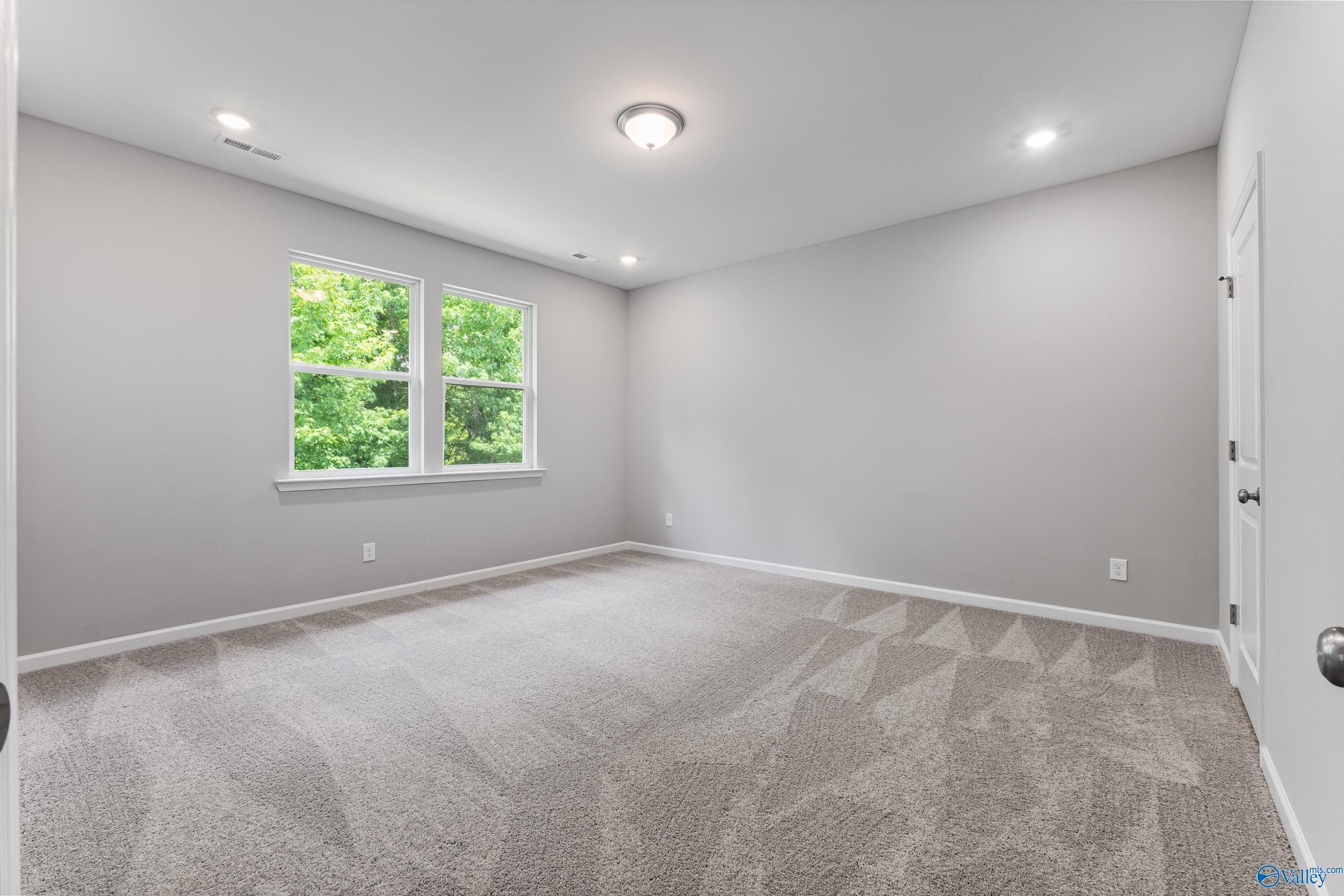 Bright empty bedroom with gray walls, plush carpet, large window overlooking trees, and recessed lighting in Davidson Homes The Phoenix, Hazel Green, Alabama