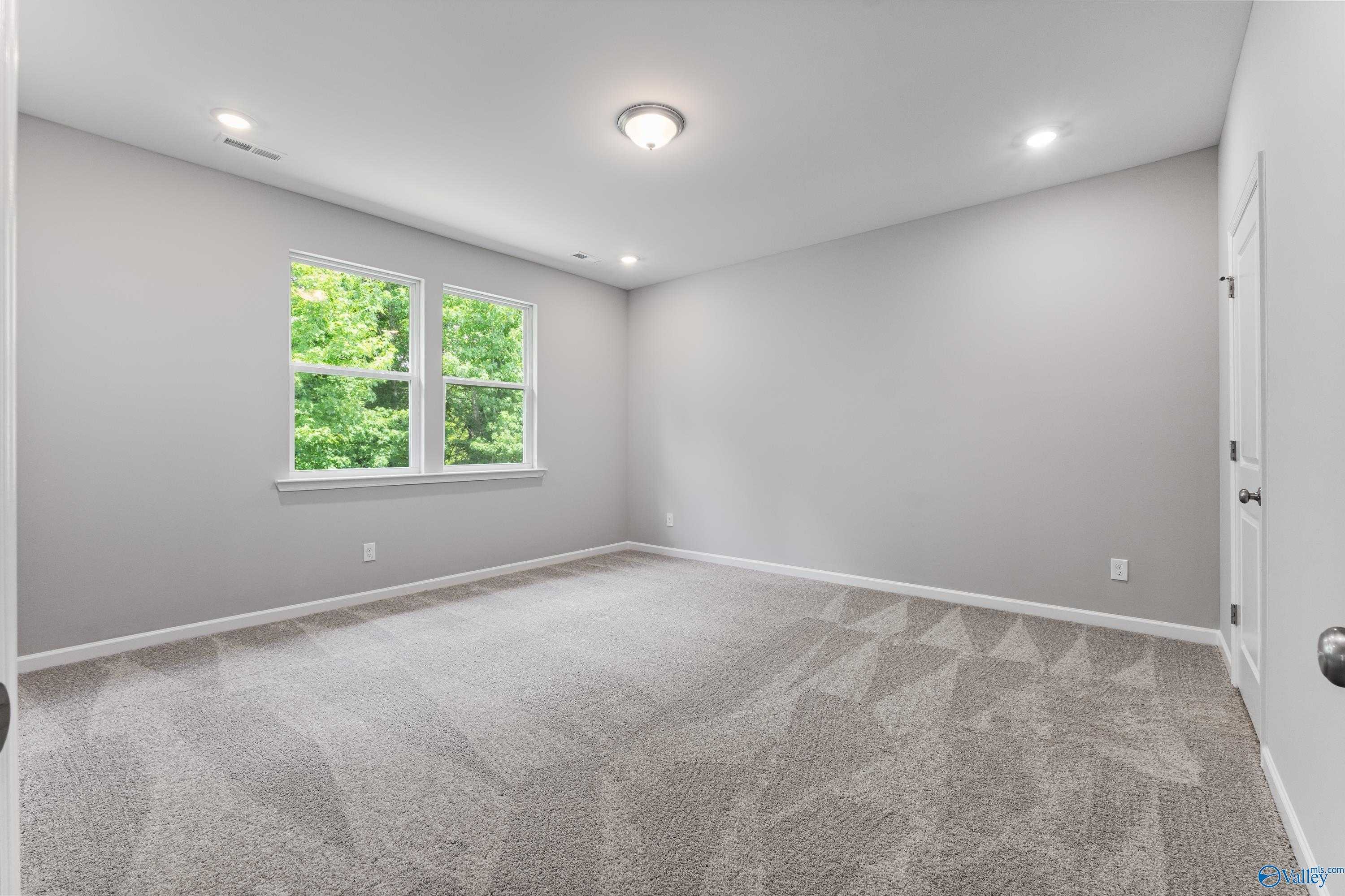 Bright secondary bedroom with large window overlooking trees, gray walls, and carpet in Davidson Homes The Phoenix, Hazel Green, AL