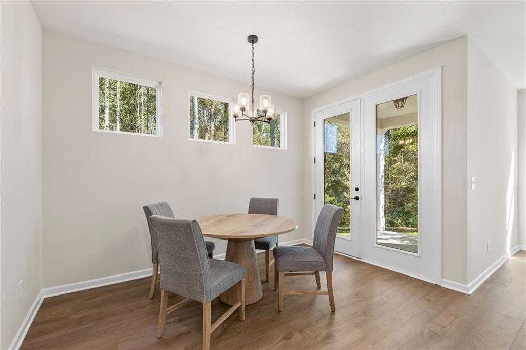 Elegant dining room with round wooden table, gray upholstered chairs, chandelier, and French doors to wooded backyard in The Daphne B, Loganville, GA