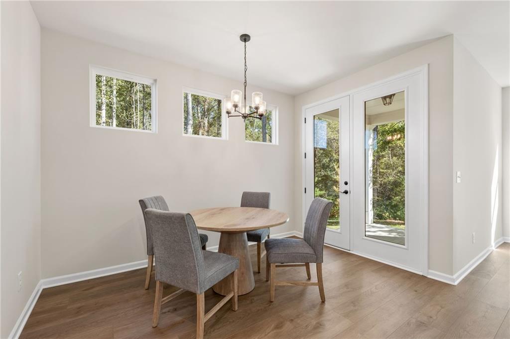 Elegant dining room with round wood table, gray upholstered chairs, chandelier, large windows, and French doors to wooded view in The Daphne B, Loganville, GA