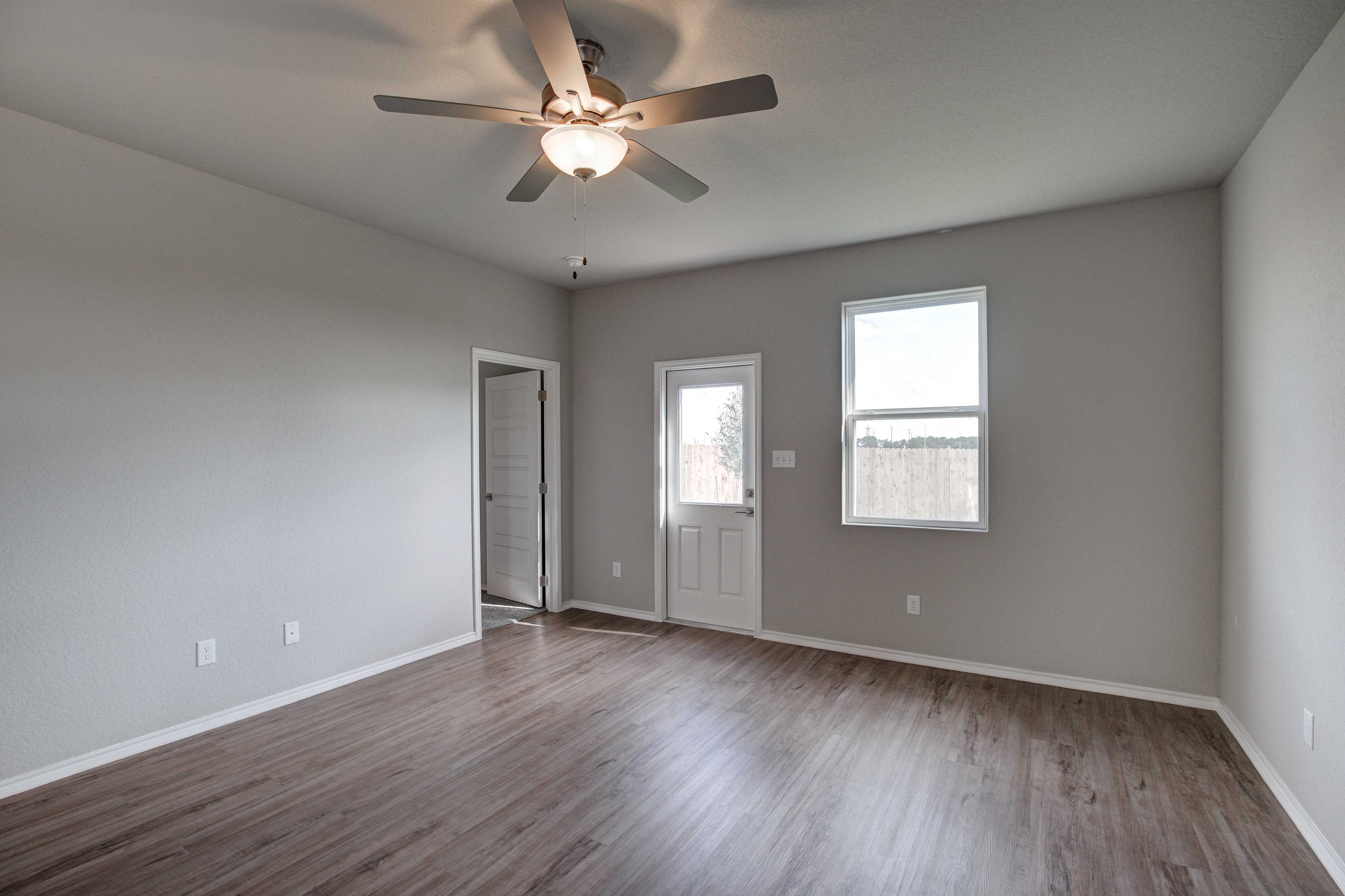 Spacious master bedroom in The Frio B with gray walls, hardwood floors, ceiling fan, and glass-paneled door to backyard