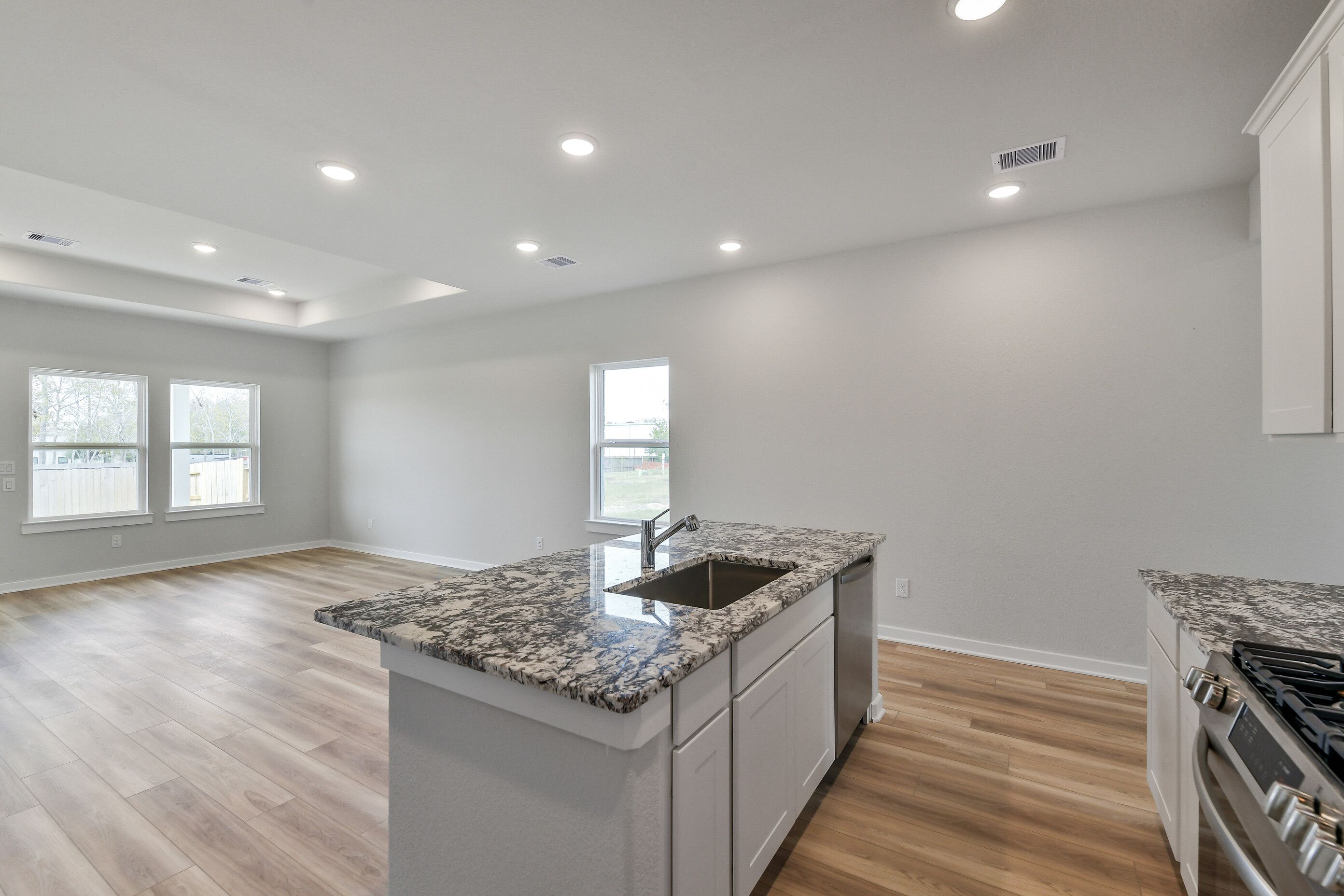 Modern kitchen island with speckled granite countertop, sink, and stainless gas range in Davidson Homes Colorado G, Magnolia TX