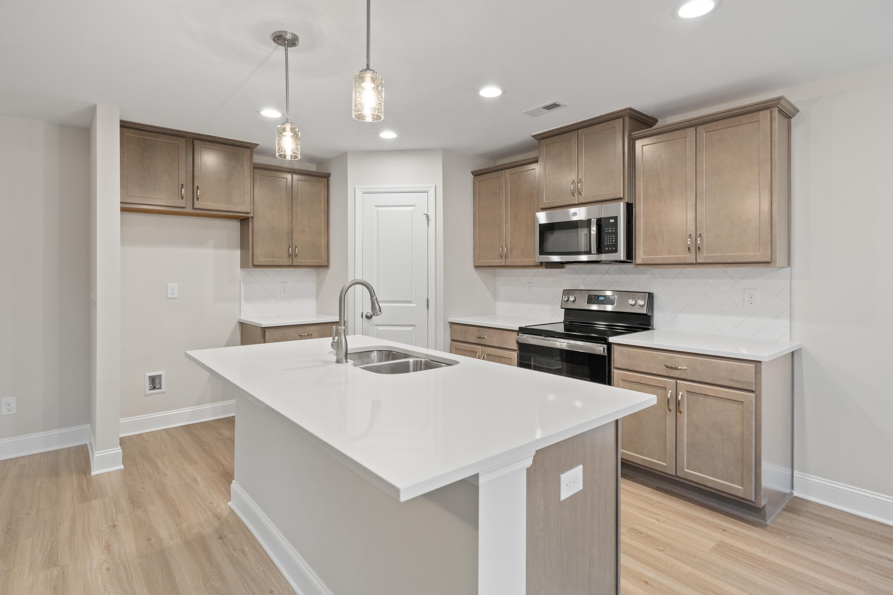 Spacious modern kitchen in The Asheville featuring white quartz island sink, shaker cabinets, stainless appliances, pendant lights