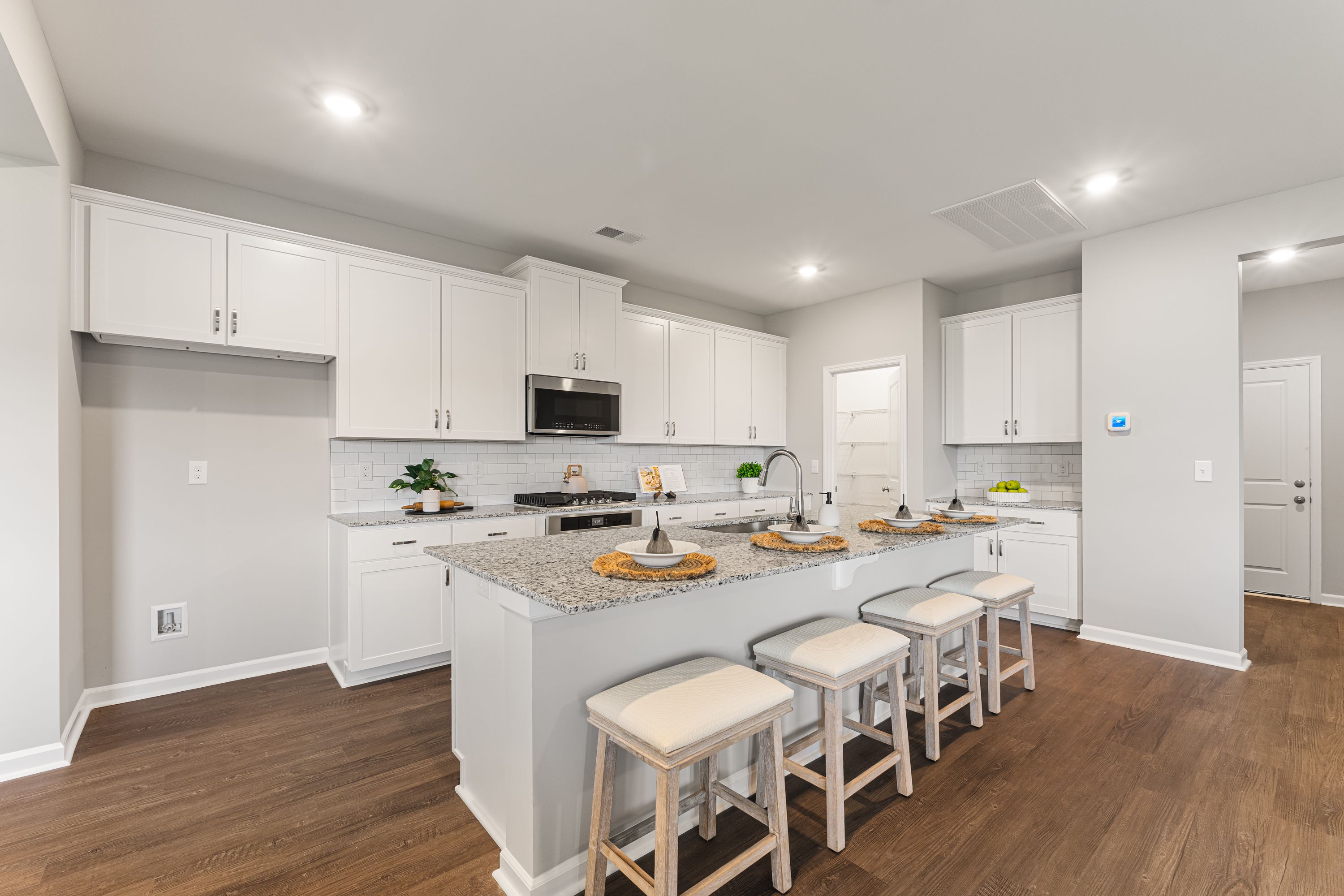 Spacious gourmet kitchen in The Avalon E featuring white shaker cabinets, granite island with bar stools, and stainless appliances