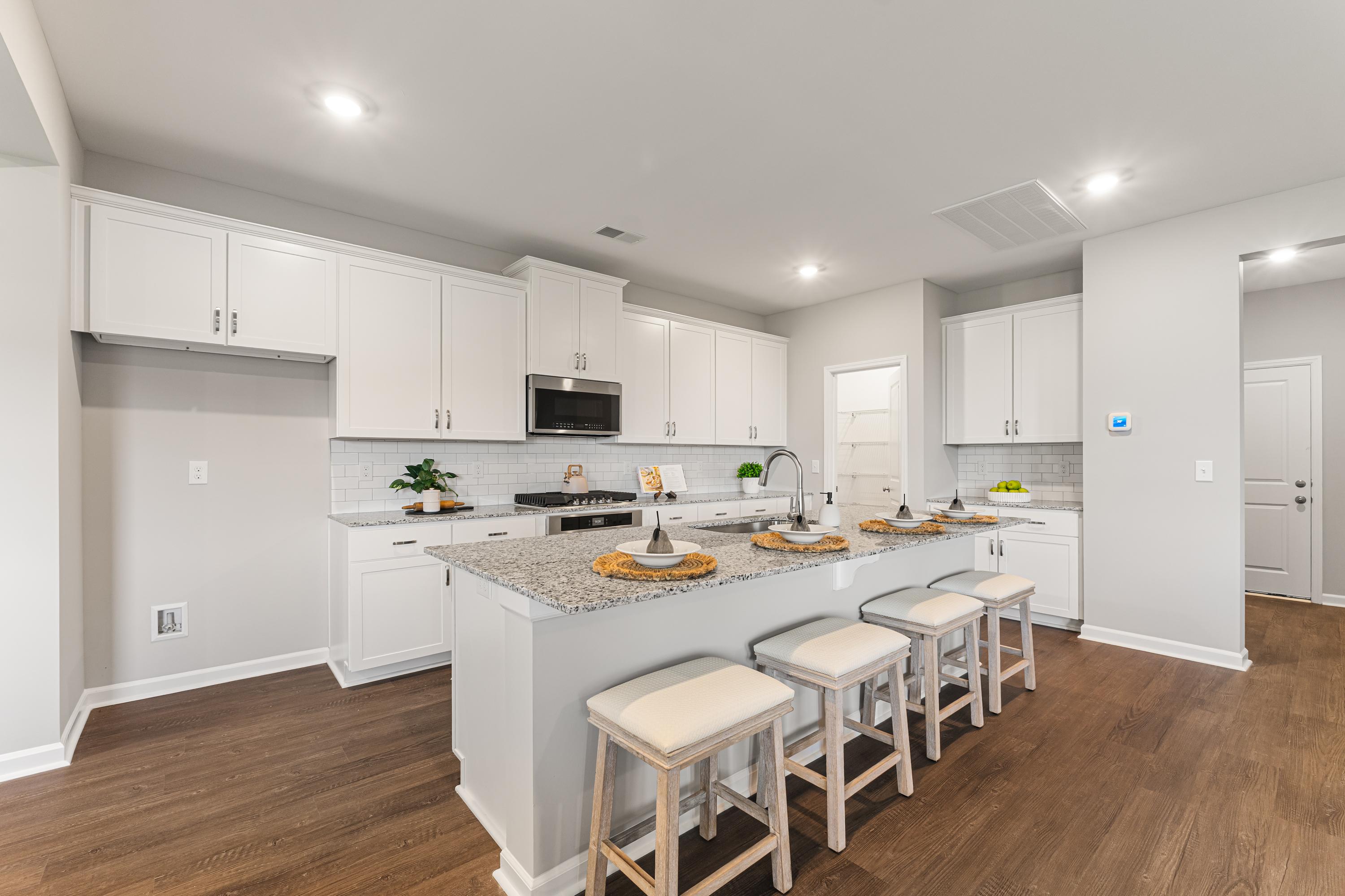 Gourmet kitchen in The Avalon D featuring white shaker cabinets, granite island with bar stools, and stainless appliances