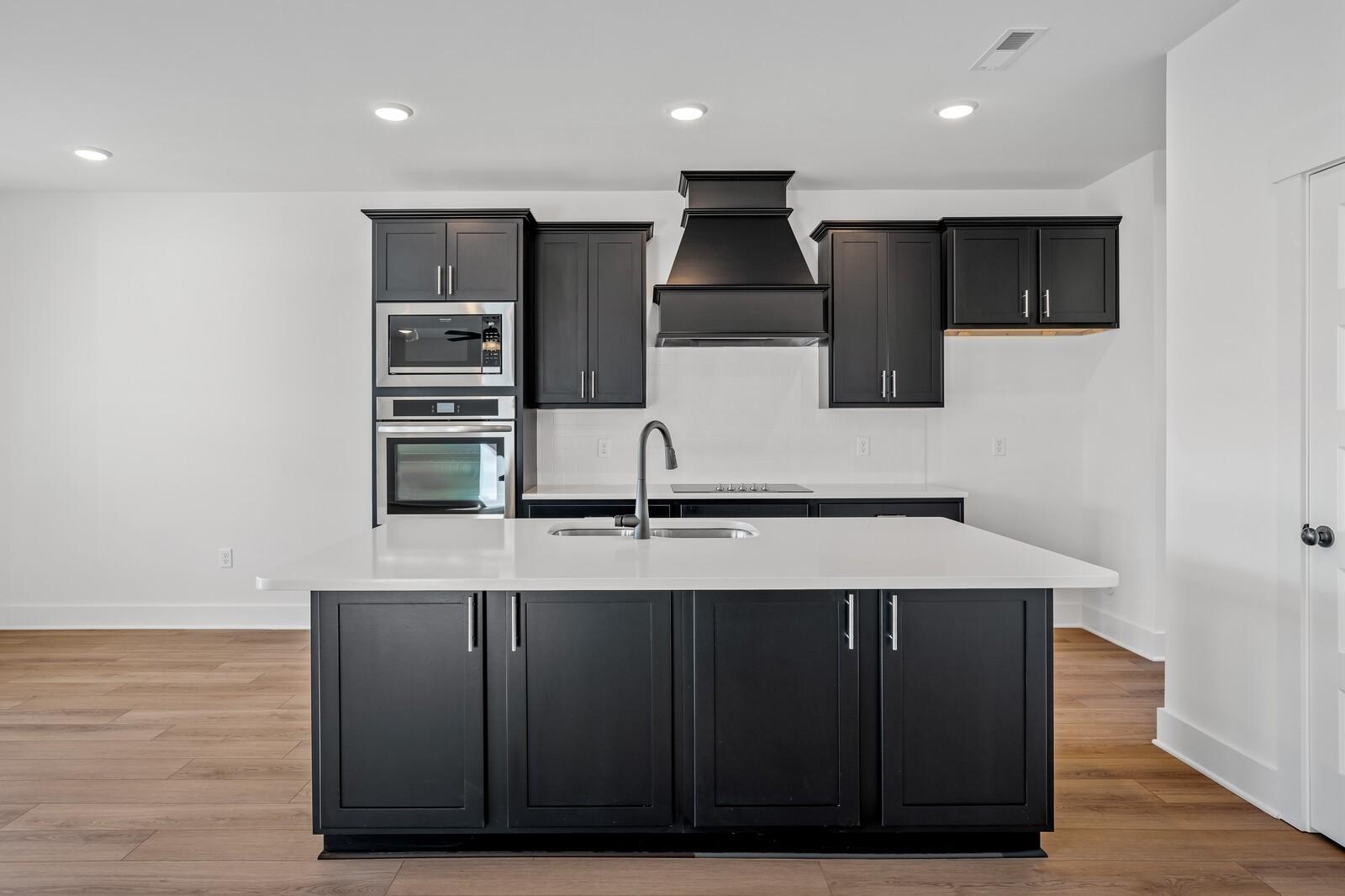 Contemporary kitchen with black shaker cabinets, white quartz island, double ovens in Davidson Homes The Willow, Gallatin TN