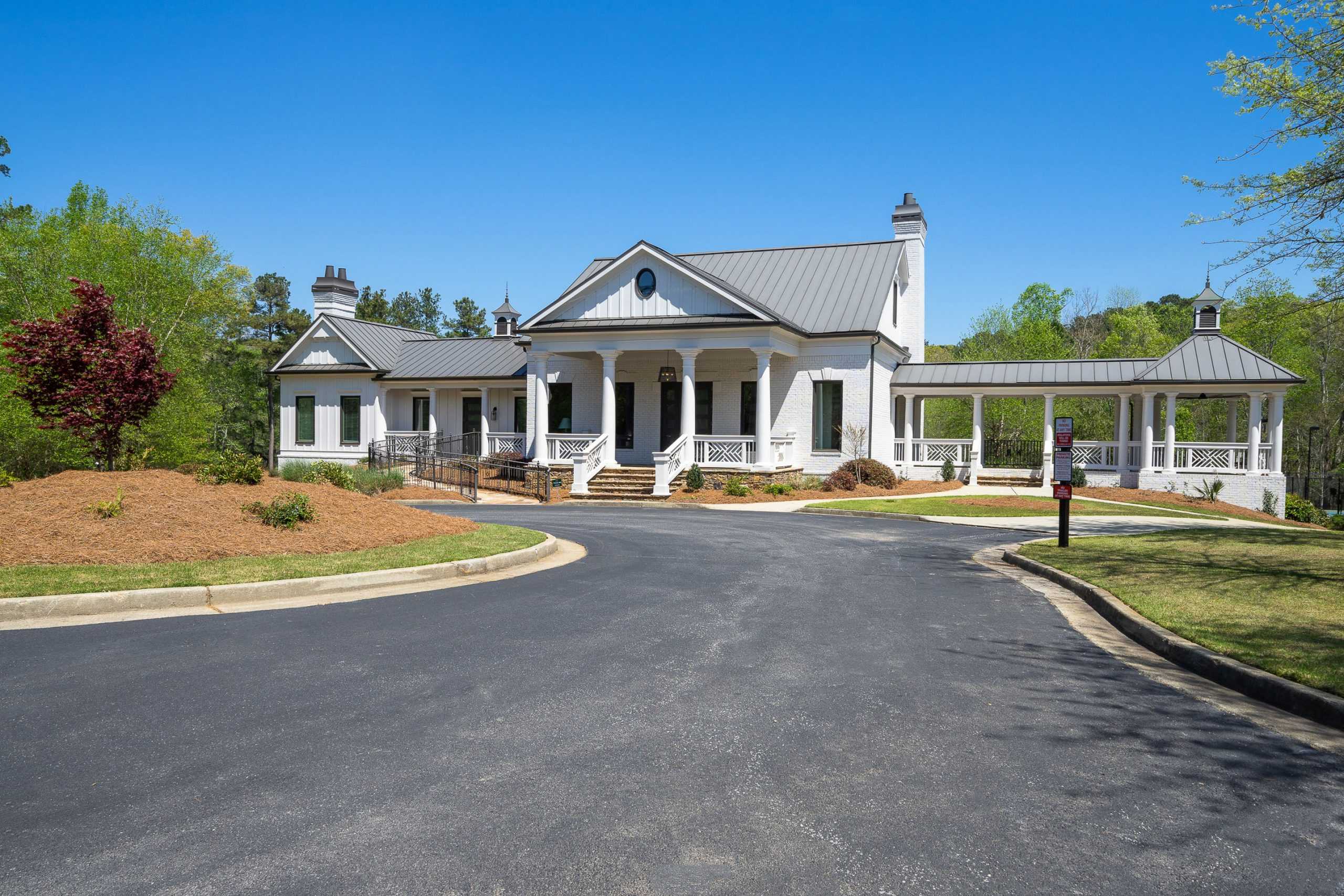 Classic white clubhouse with columned porches and metal roof at Riverwood in Dallas Georgia amid lush trees and curved driveway