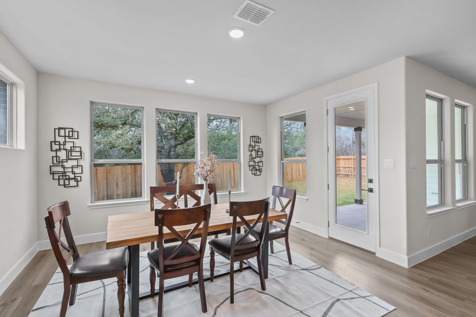 Bright dining area in The Belmont J featuring a wooden table, cross-back chairs, and large windows with backyard views.