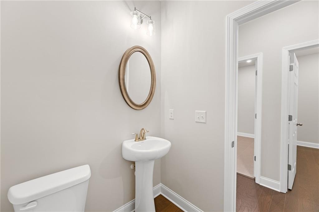 Elegant powder room with white pedestal sink, round gold-framed mirror, and neutral walls in Davidson Homes The Harrison G, Hoschton, Georgia