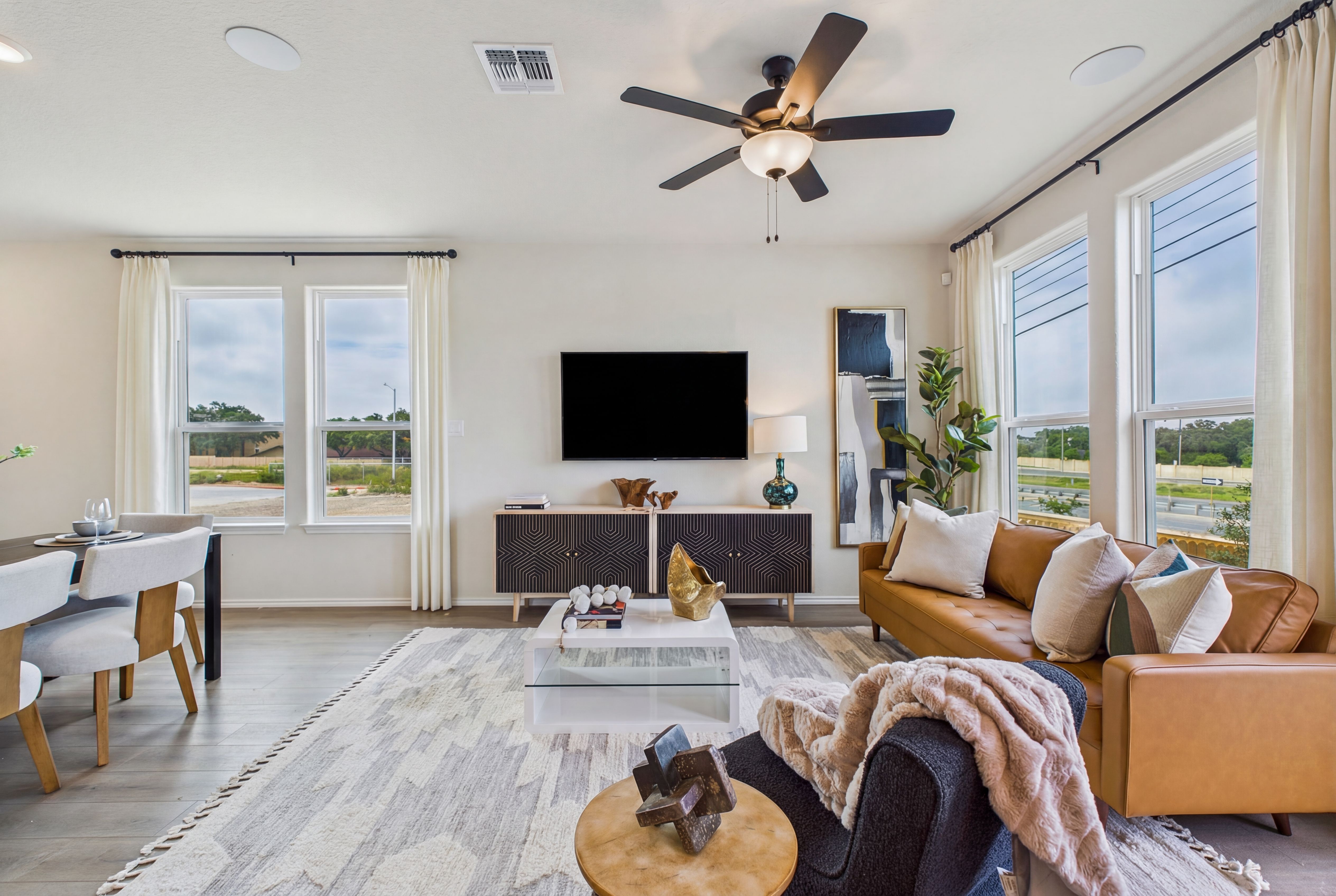 Spacious open-concept living room at Meadows at Oak Creek in San Antonio Texas with large windows, leather sofa, and modern decor