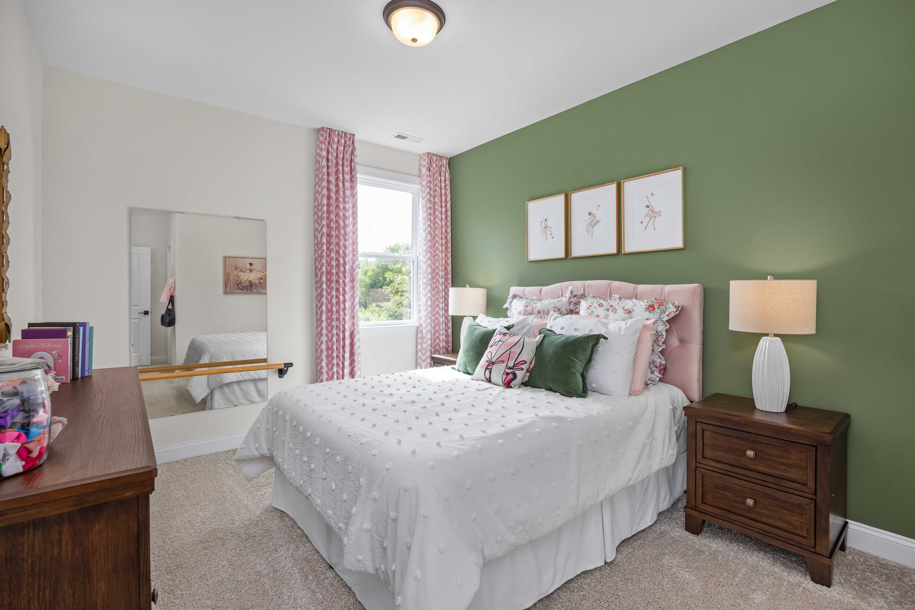 Cozy girl's bedroom at Laneridge Estates in Raleigh NC with white tufted bed, pink green pillows, vanity mirror, and green accent wall