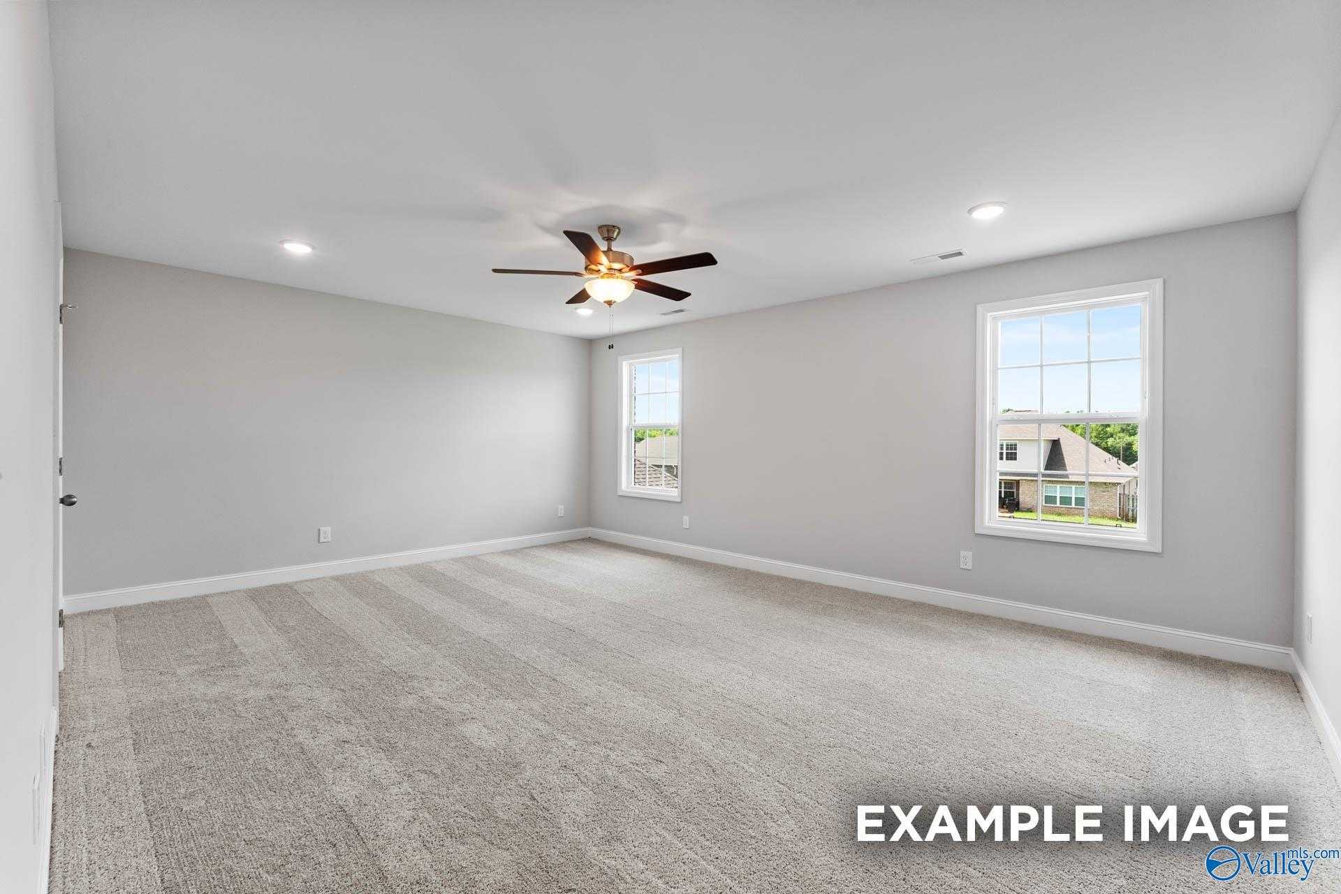 Spacious bedroom with light gray walls, beige carpet, ceiling fan, and double windows overlooking greenery in Davidson Homes The Madison A, Harvest, Alabama