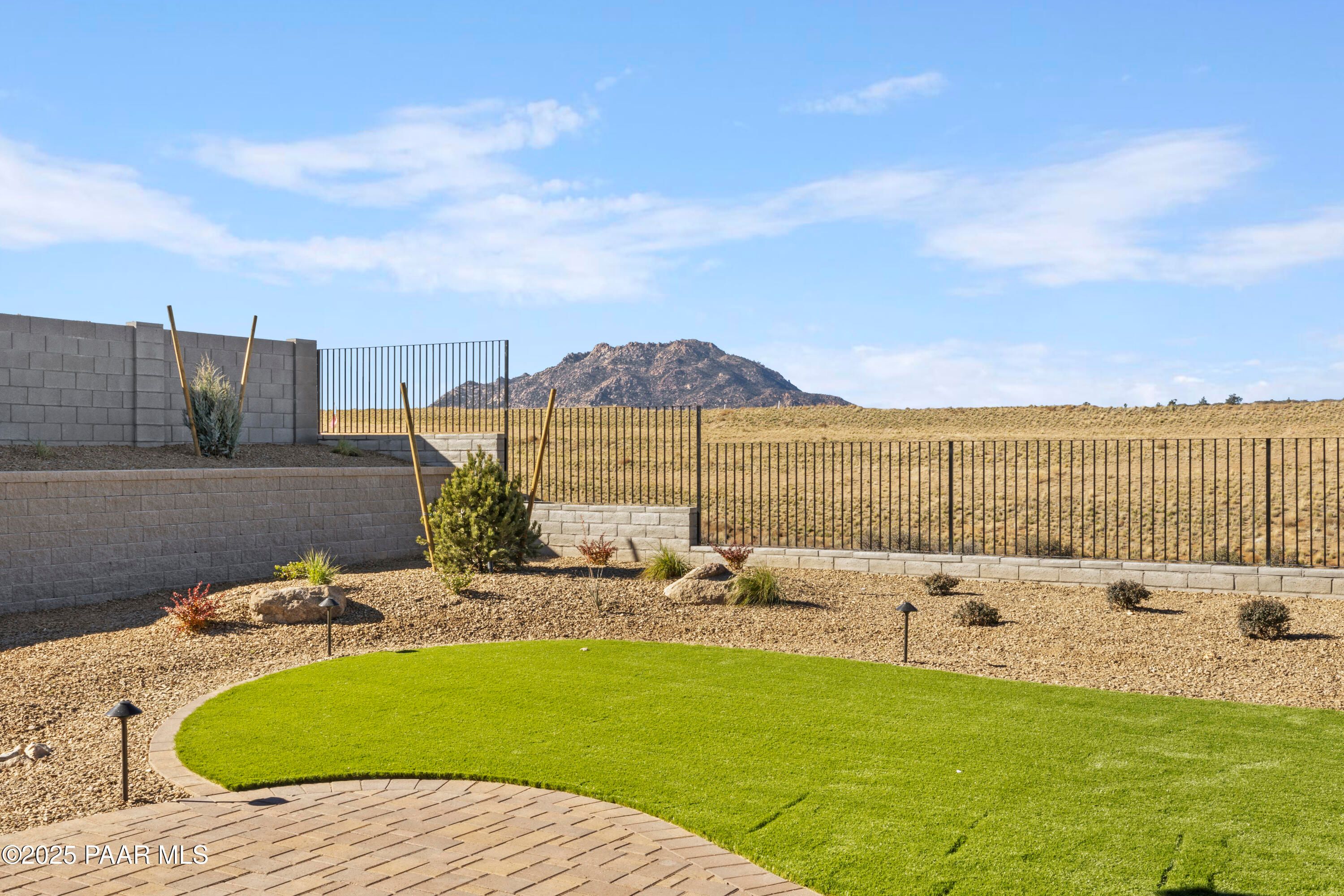Private backyard with curved synthetic turf lawn, desert plants, paver path, and mountain view in Hidden Hills, Prescott, Arizona