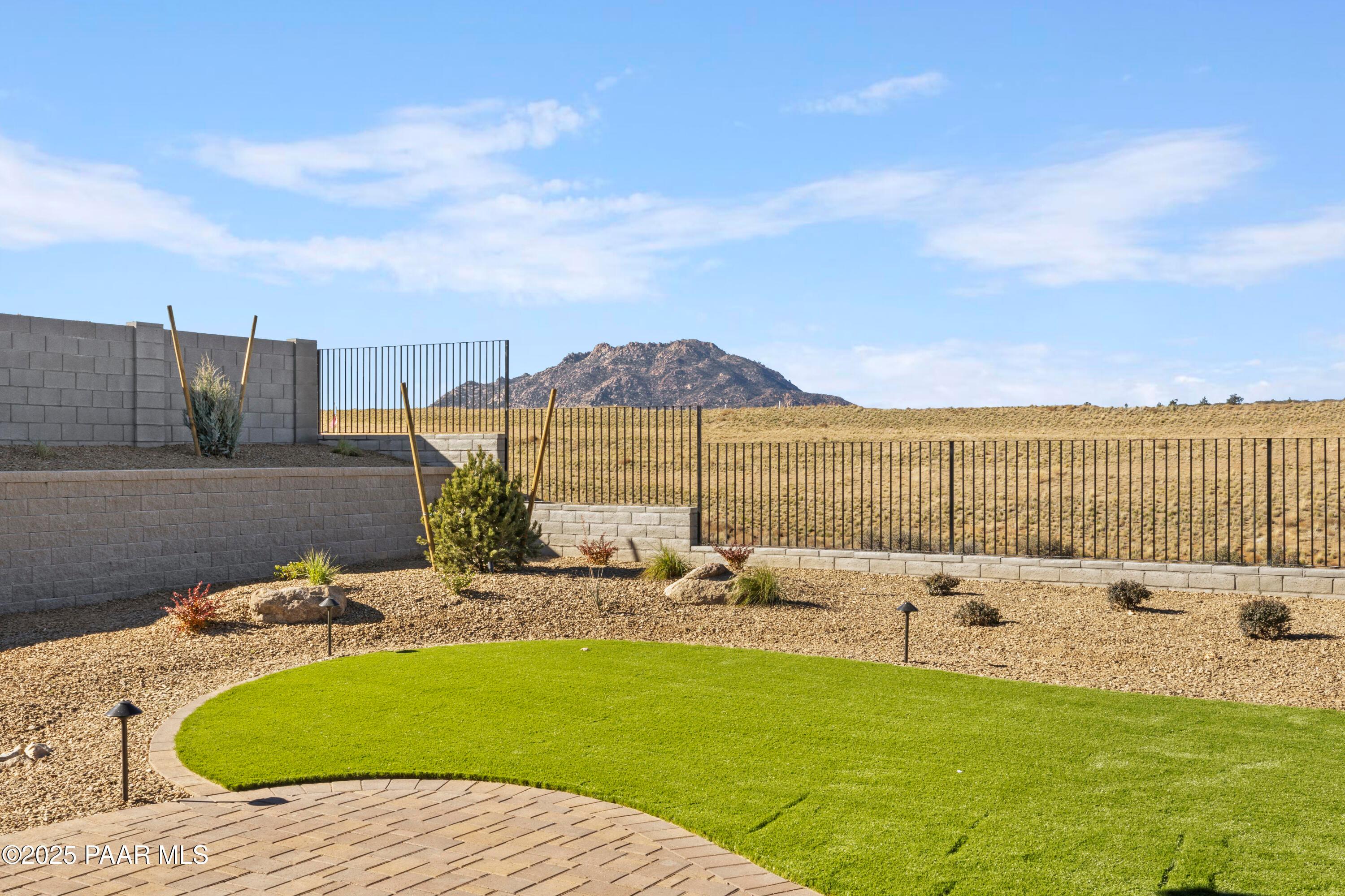 Private backyard with curved synthetic turf lawn, desert plants, paver path, and mountain view in Hidden Hills, Prescott, Arizona