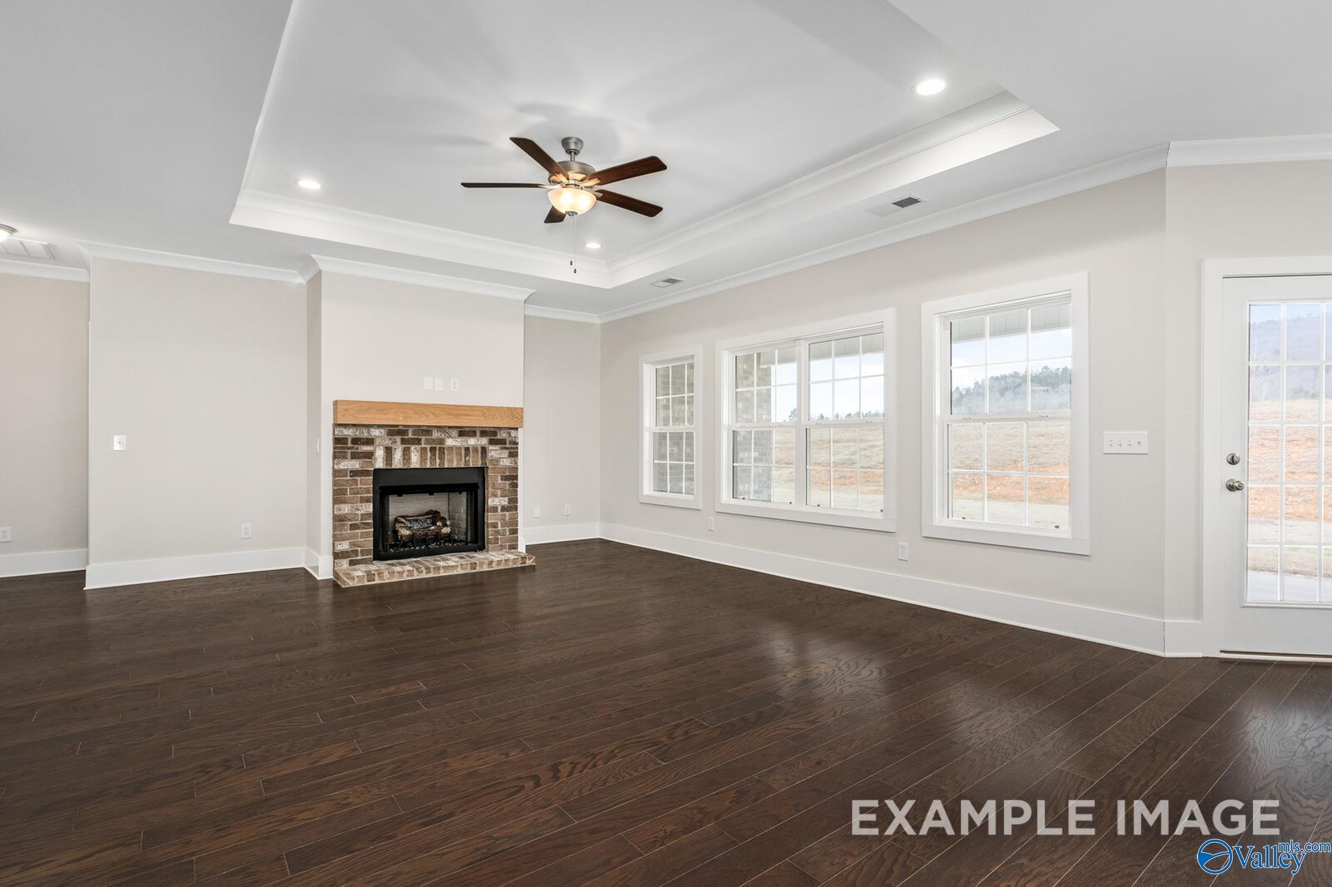 Cozy living room with brick gas fireplace, large windows, ceiling fan, and hardwood floors in Davidson Homes The Rockford, Harvest, AL