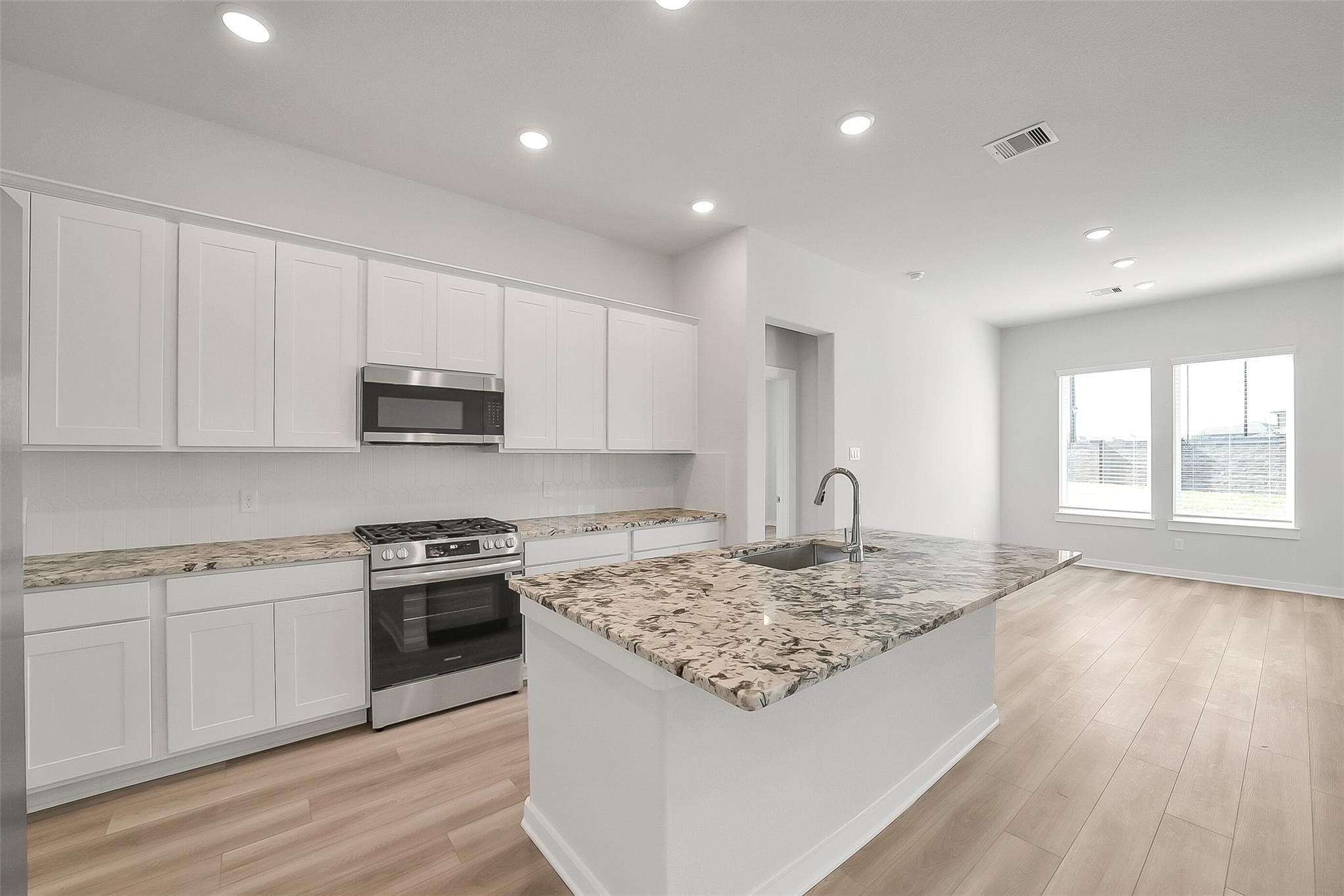 Open-concept kitchen with white shaker cabinets, granite island, stainless appliances in Davidson Homes Acadia A, Sunterra Katy TX