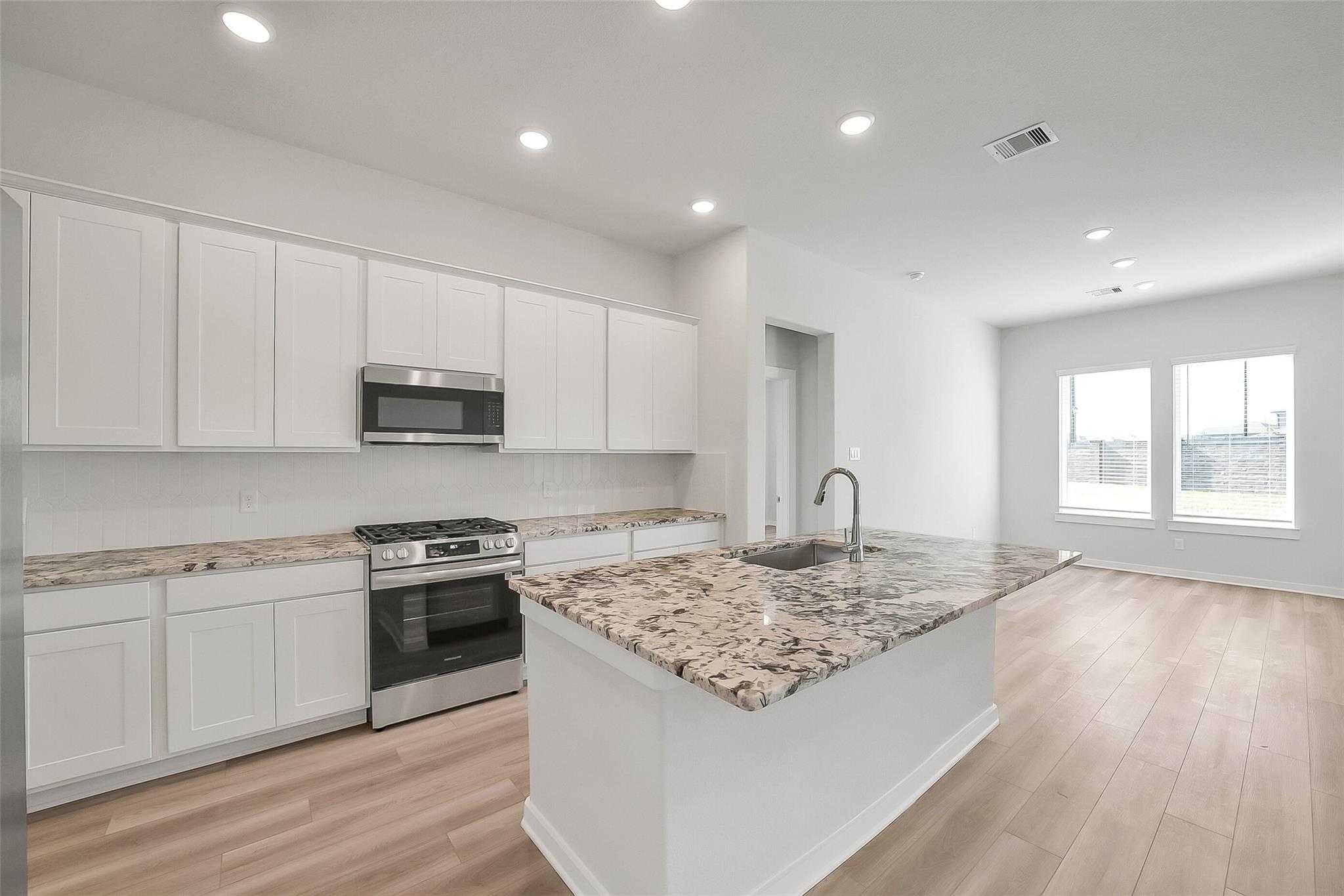 Open-concept kitchen with white shaker cabinets, granite island, stainless appliances in Davidson Homes Acadia A, Sunterra Katy TX