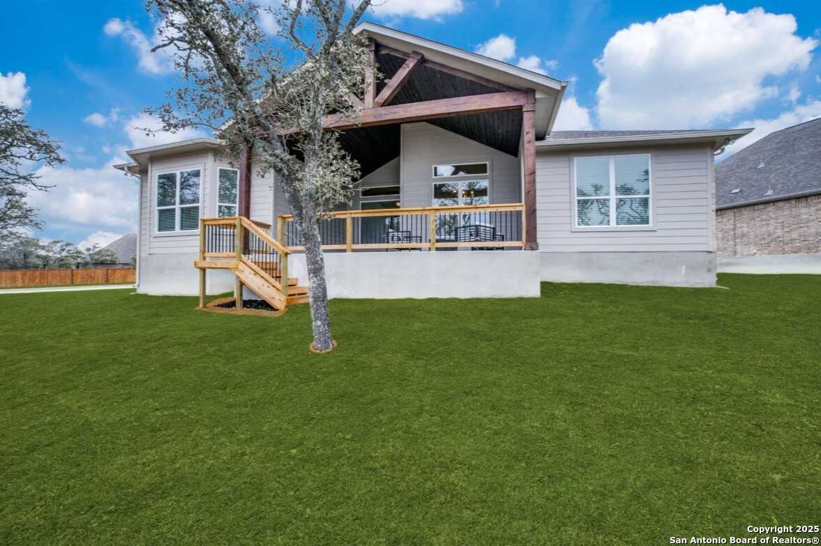 Covered back patio with exposed wooden beams, metal railing, and stairs to lush green yard in The Garner B home, Ladera, San Antonio