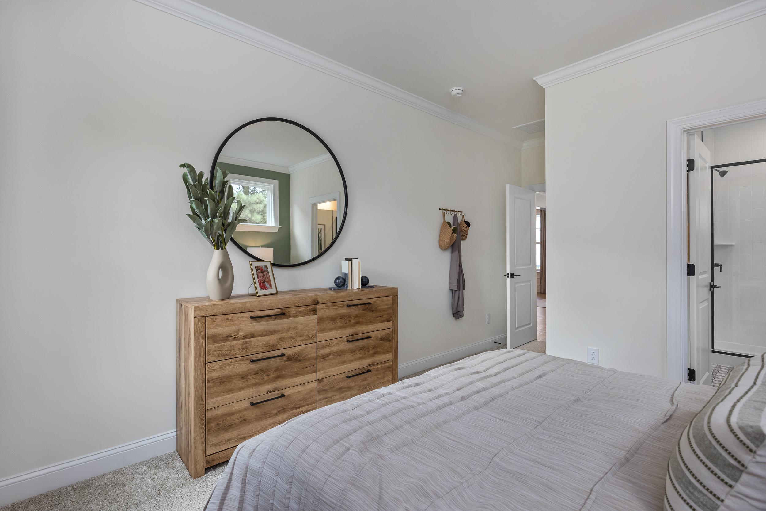Spacious bedroom at Laneridge Estates in Raleigh NC with wooden dresser, round mirror, king bed, and en-suite bath