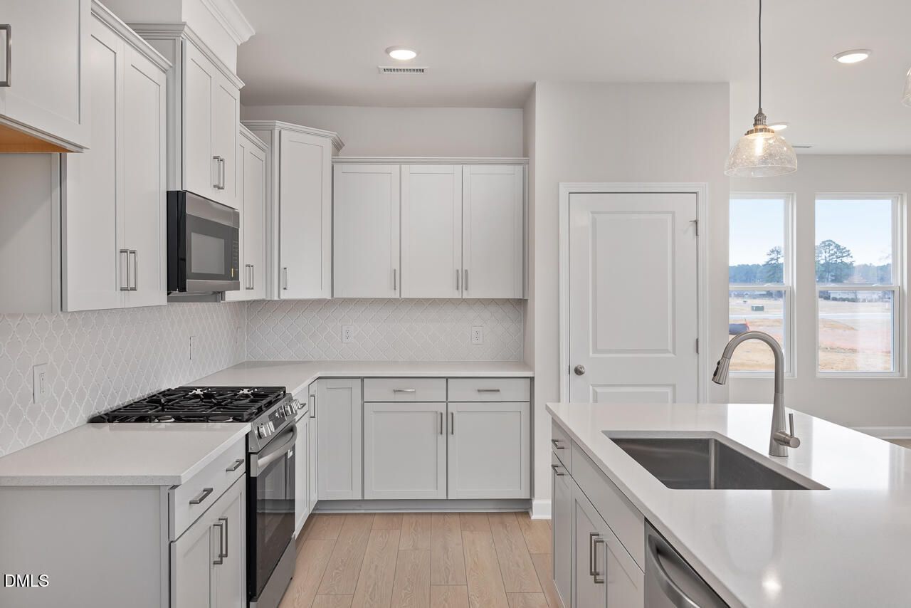 Modern white kitchen with stainless appliances, quartz island, subway tile backsplash in The Daphne C by Davidson Homes, Lillington, NC