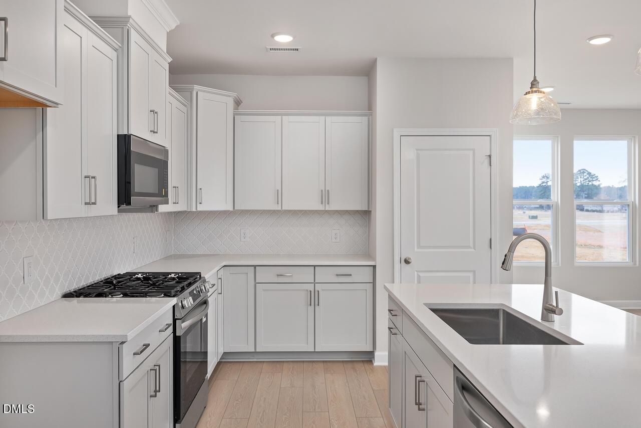 Modern white kitchen with stainless appliances, quartz island, subway tile backsplash in The Daphne C by Davidson Homes, Lillington, NC