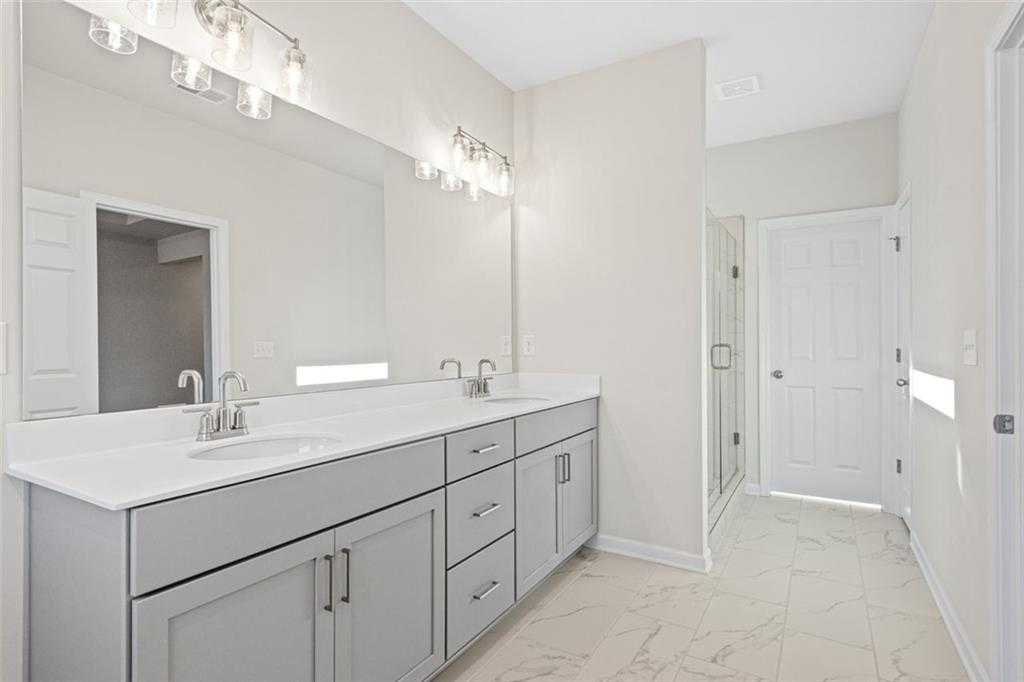 Modern master bathroom featuring double vanity with gray cabinets, dual sinks, and glass shower door in Davidson Homes The Glenwood C, Hoschton, GA