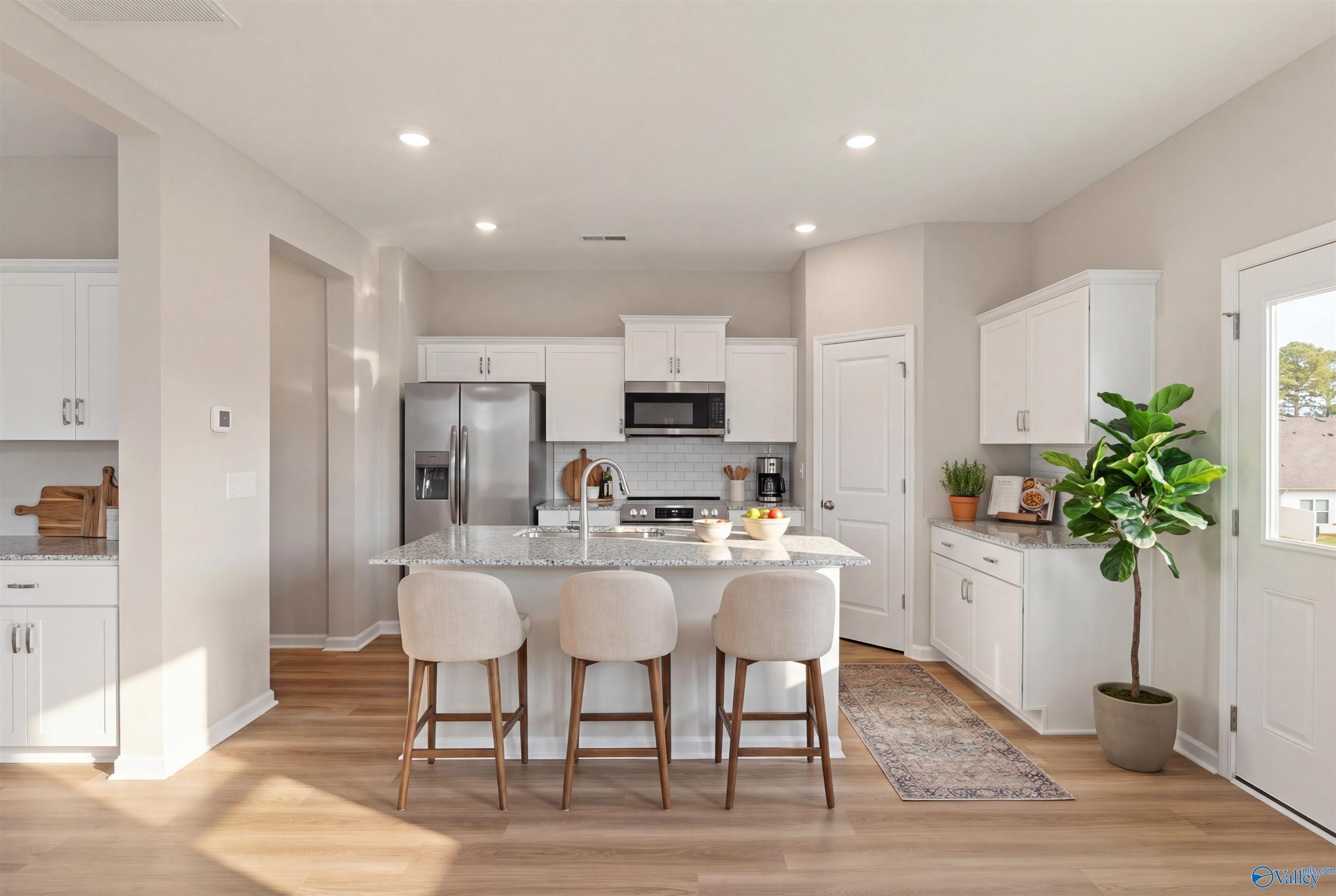 Modern white kitchen with quartz island, bar stools, stainless appliances, and plants in The Augusta floor plan, Davidson Homes, Madison AL