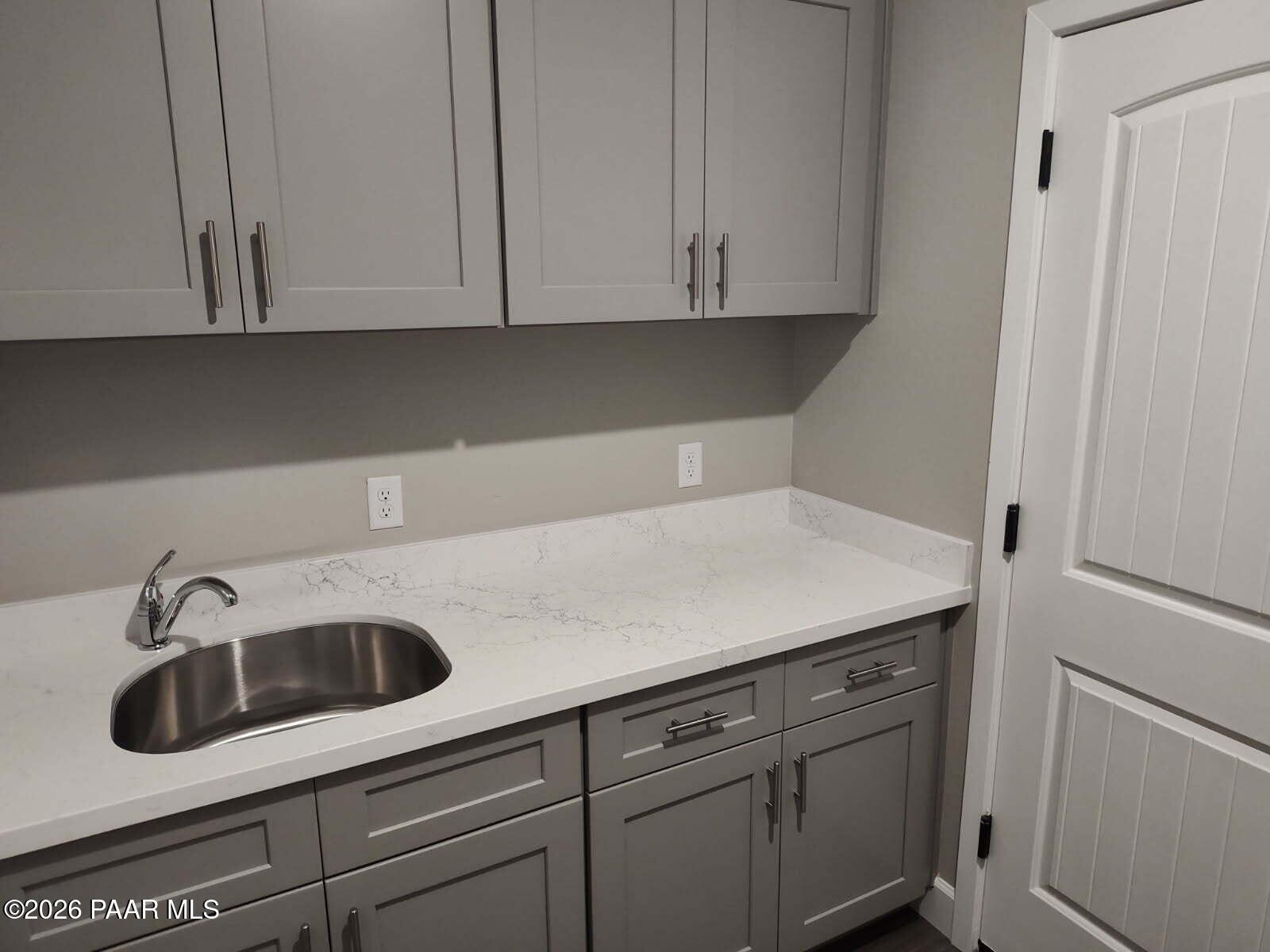 Modern laundry room featuring gray shaker cabinets, white quartz countertop, stainless sink in Davidson Homes The Harmony C, Prescott Valley