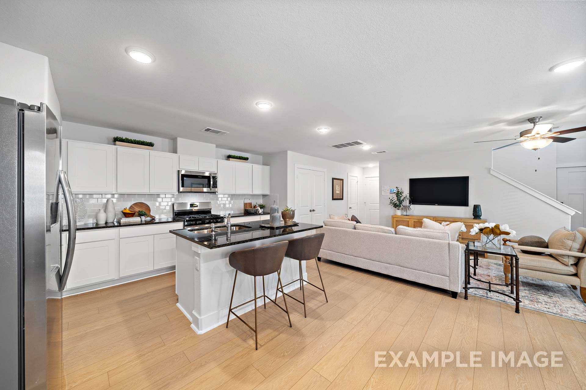 Open-concept kitchen and living area in The Rose B home design with white cabinets, large island, stainless appliances, and beige sofa