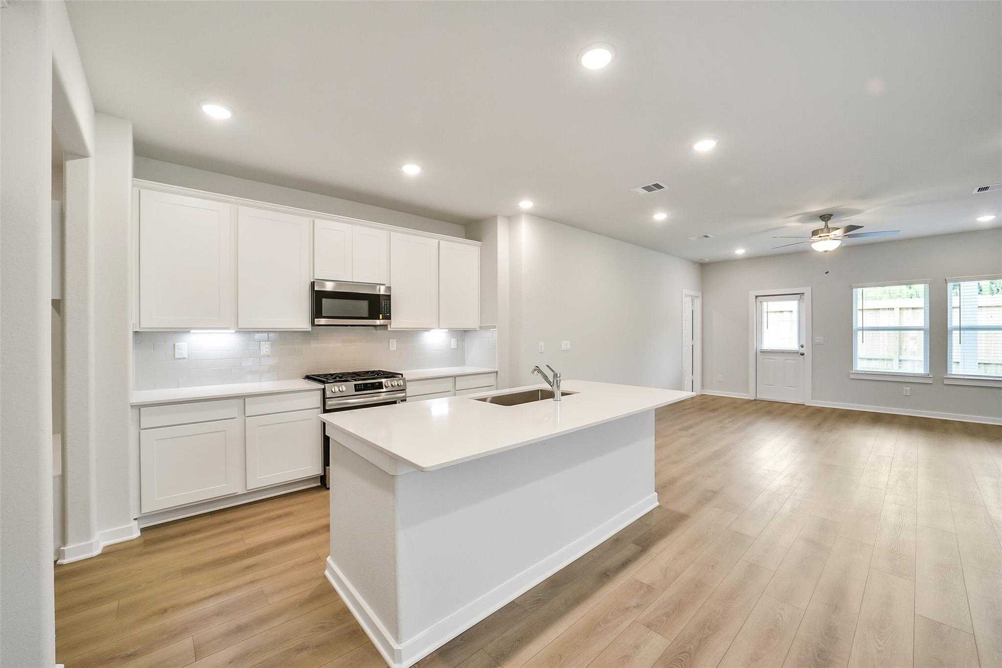 Modern white kitchen with quartz island, stainless appliances, and open living space in Davidson Homes The Blanco E, Magnolia, Texas