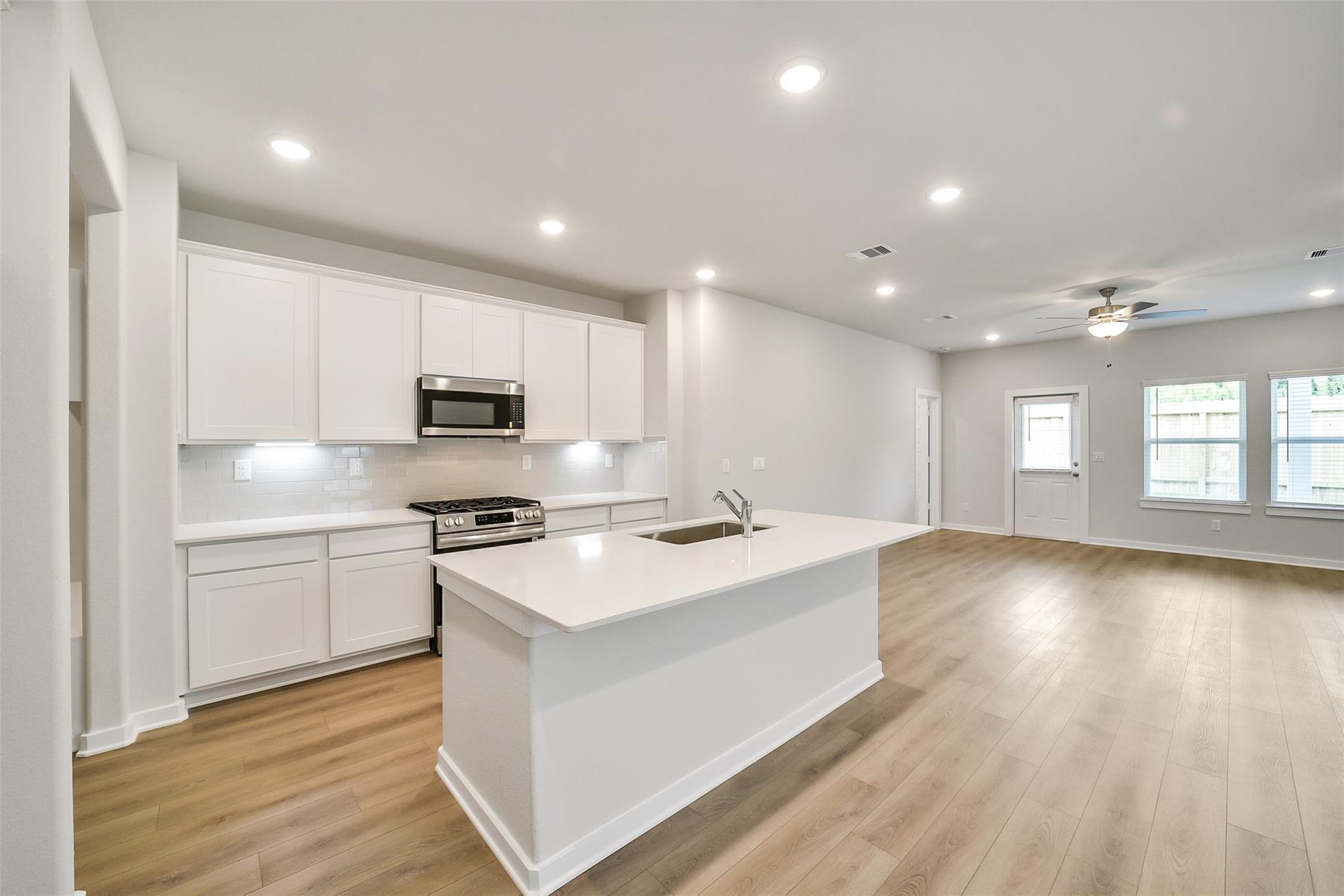 Modern white kitchen with quartz island, stainless appliances, and open living space in Davidson Homes The Blanco E, Magnolia, Texas