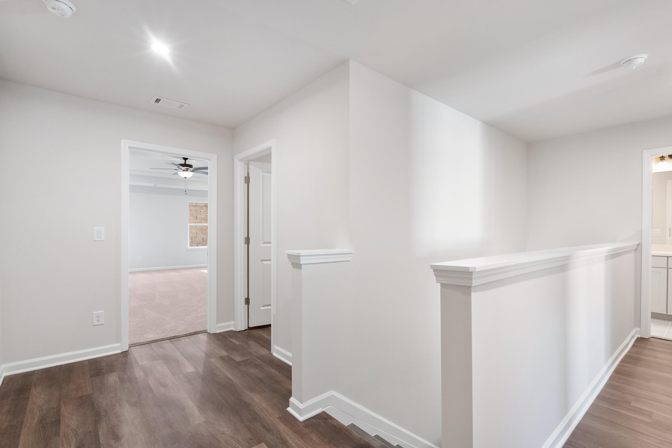 Spacious upstairs hallway in The Cary B featuring white walls, hardwood floors, open railing, bedroom doorway, and adjacent bathroom vanity