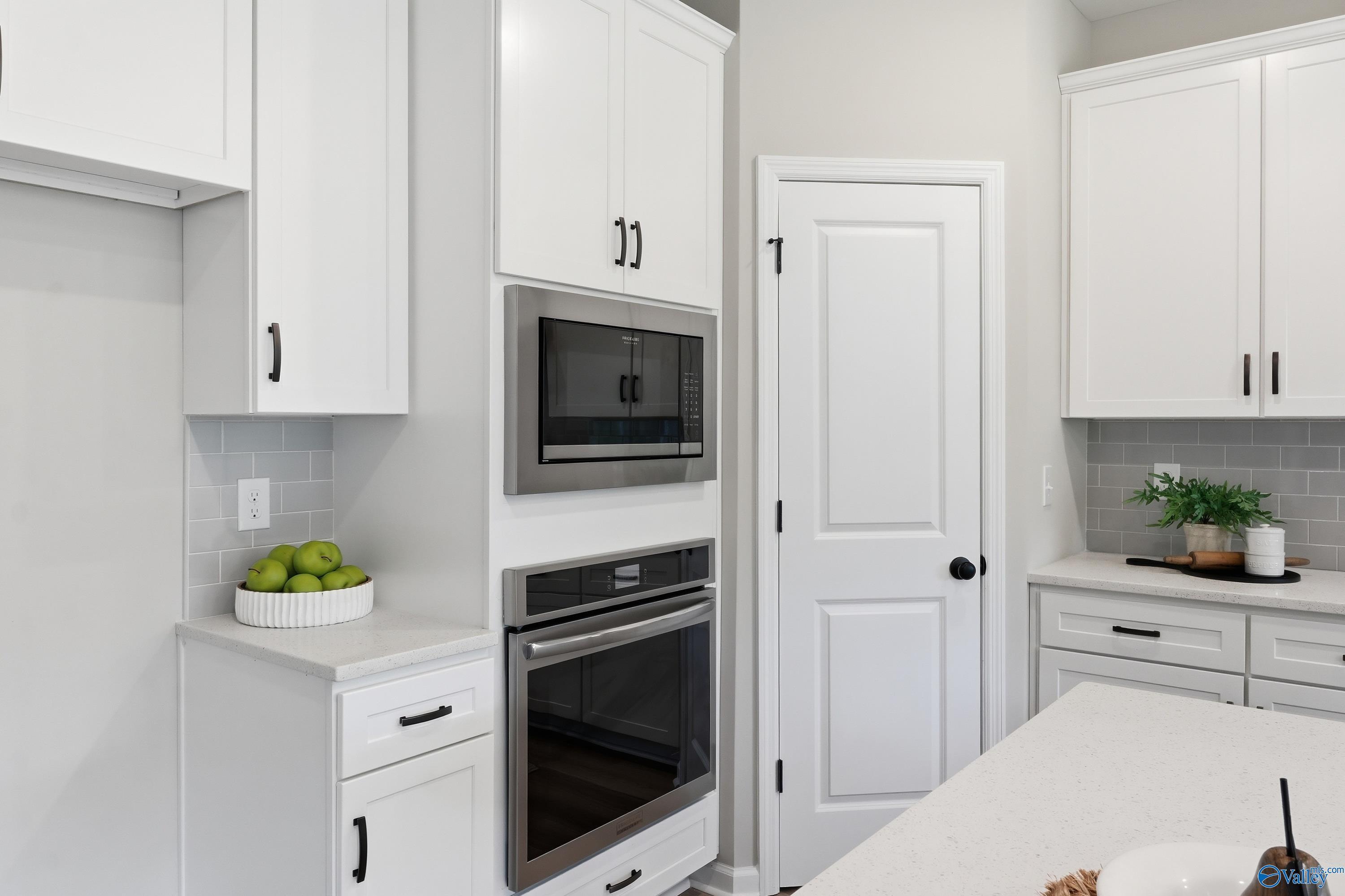 Modern white shaker kitchen with stainless double oven, microwave, gray subway backsplash, quartz counters, and fresh apples in Davidson Homes The Dorado, Huntsville AL
