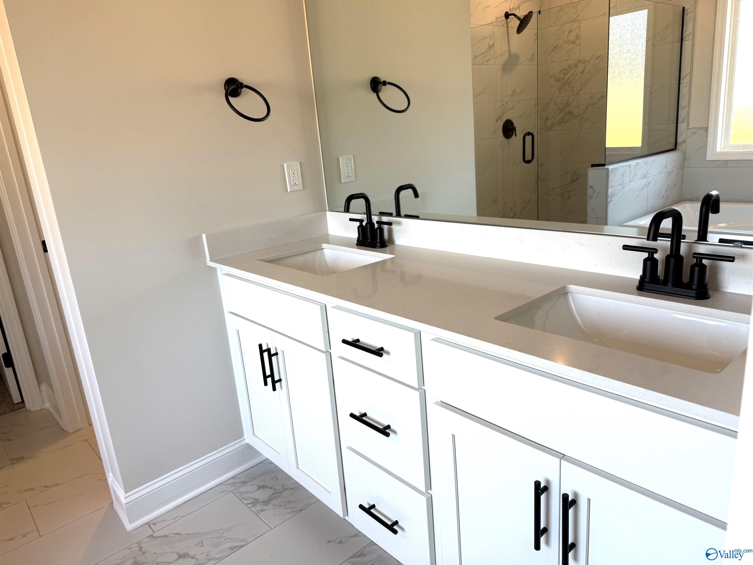 Modern master bath double vanity with white shaker cabinets, quartz counters, black faucets, and glass shower in Davidson Homes The Rockford B, Hartselle, AL