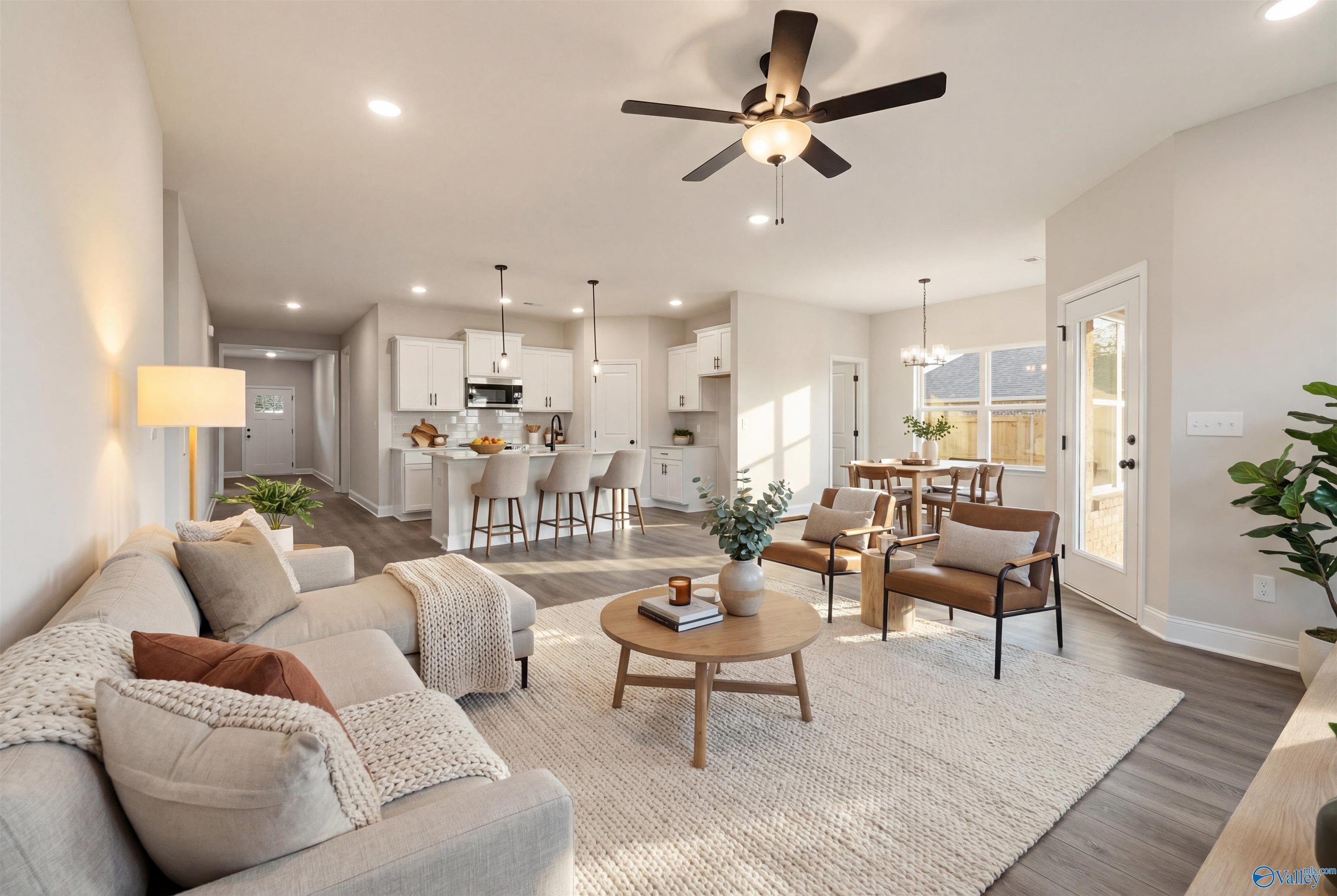 Open-concept living room with plush sofa, ceiling fan, and adjacent white kitchen in Davidson Homes The Daphne D, Arab, Alabama