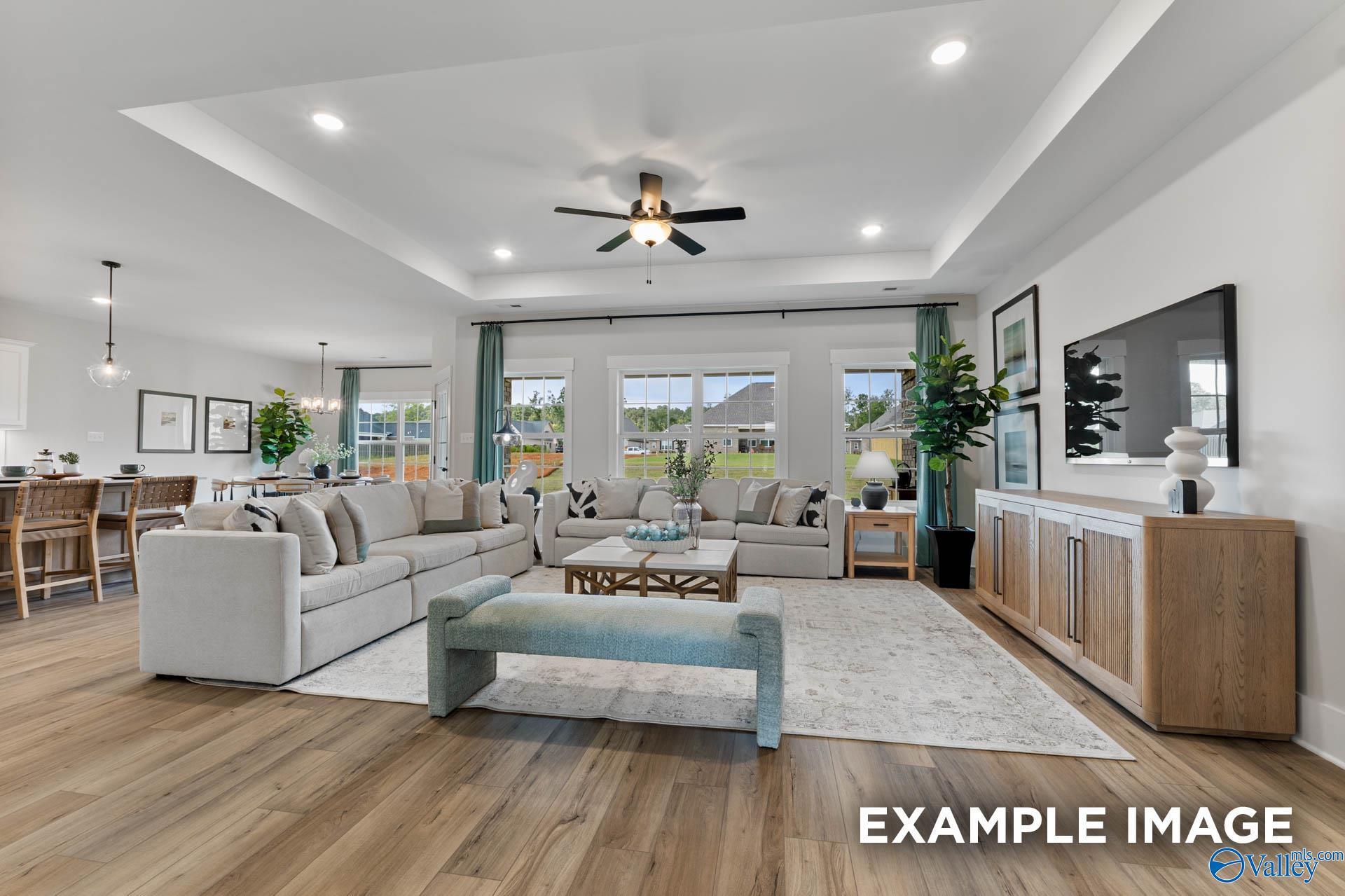 Spacious living room with L-shaped sofa, mounted TV, ceiling fan, and hardwood floors in Davidson Homes The Rockford C, Madison, Alabama